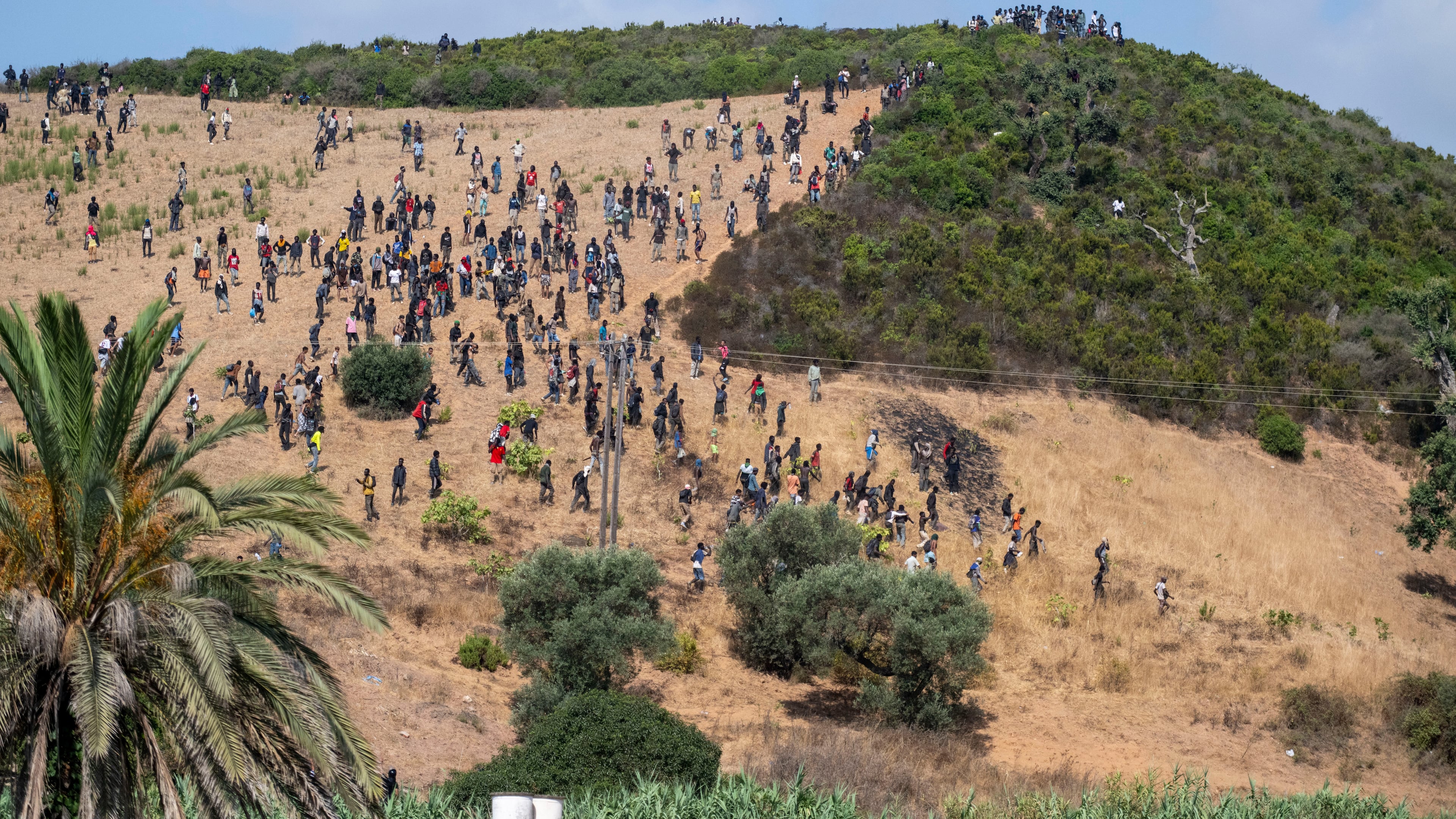Migrants gather on a hill as they attempt crossing from the border town of Fnideq to the Spanish enclave of Ceuta, Saturday, Aug. 15, 2026. (AP Photo)
