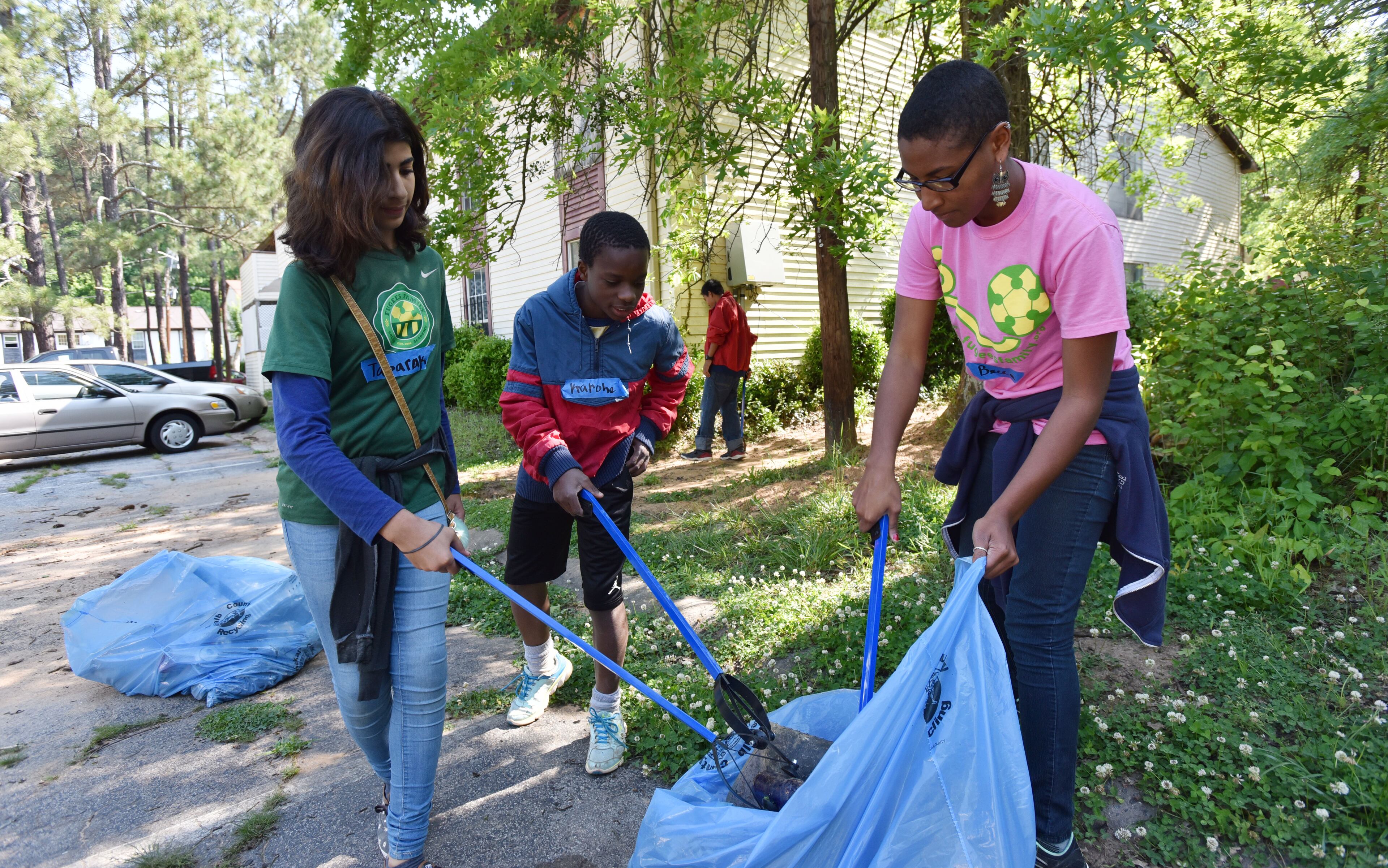 Becca Johnson (right) with young volunteers from Fugees Family soccer academy, Tabarak Tamer (left), 12, and Karohe Dumant, 12, clean up at Brannon Hill Condominiums in DeKalb County on Saturday, May 7, 2016. HYOSUB SHIN / HSHIN@AJC.COM
