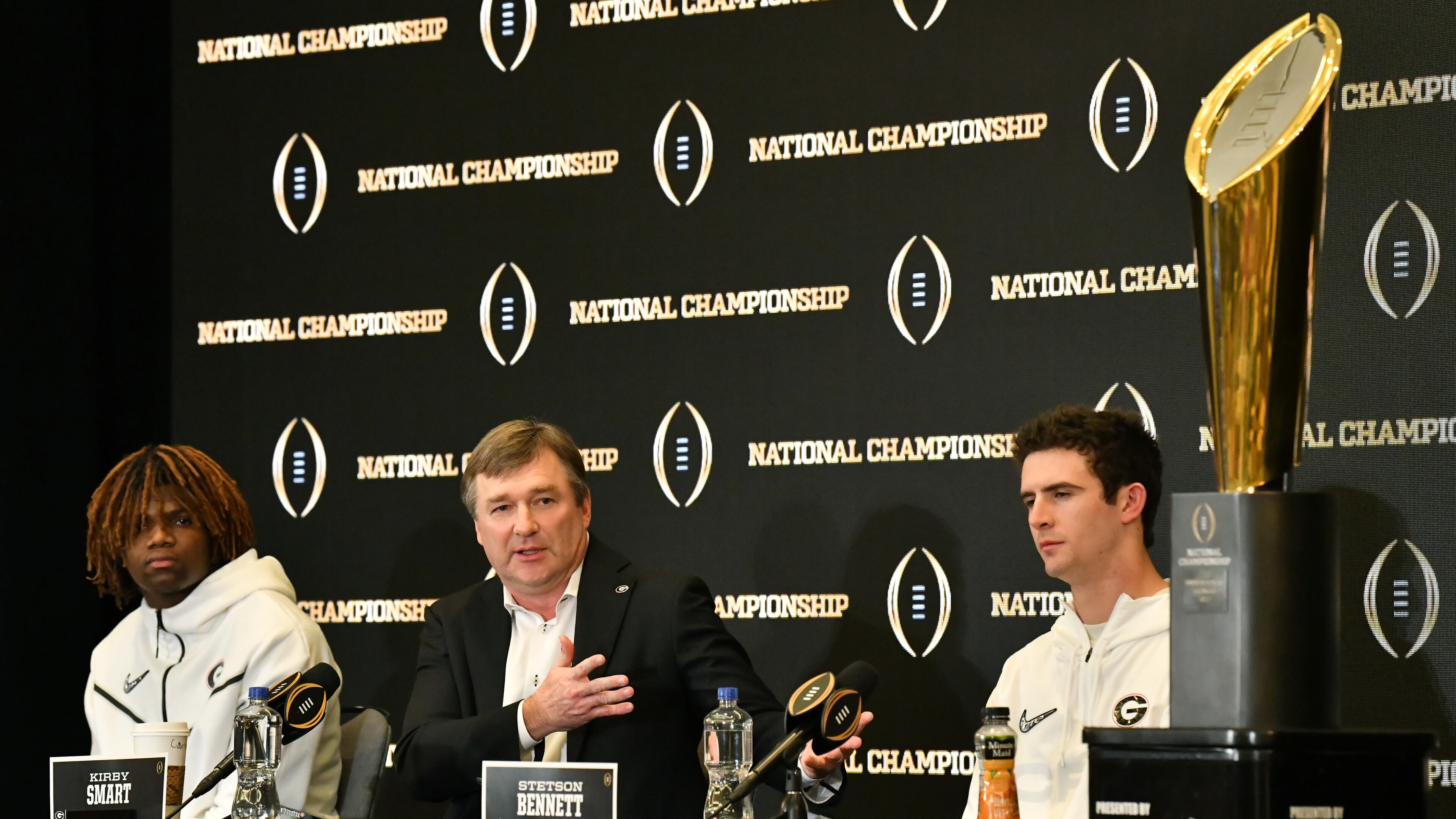 January 11, 2022 Indianapolis, IN - Georgia's head coach Kirby Smart speaks as defensive back Lewis Cine and quarterback Stetson Bennett sit next during Champions News Conference in Indianapolis on Tuesday, January 11, 2022. (Hyosub Shin / Hyosub.Shin@ajc.com)