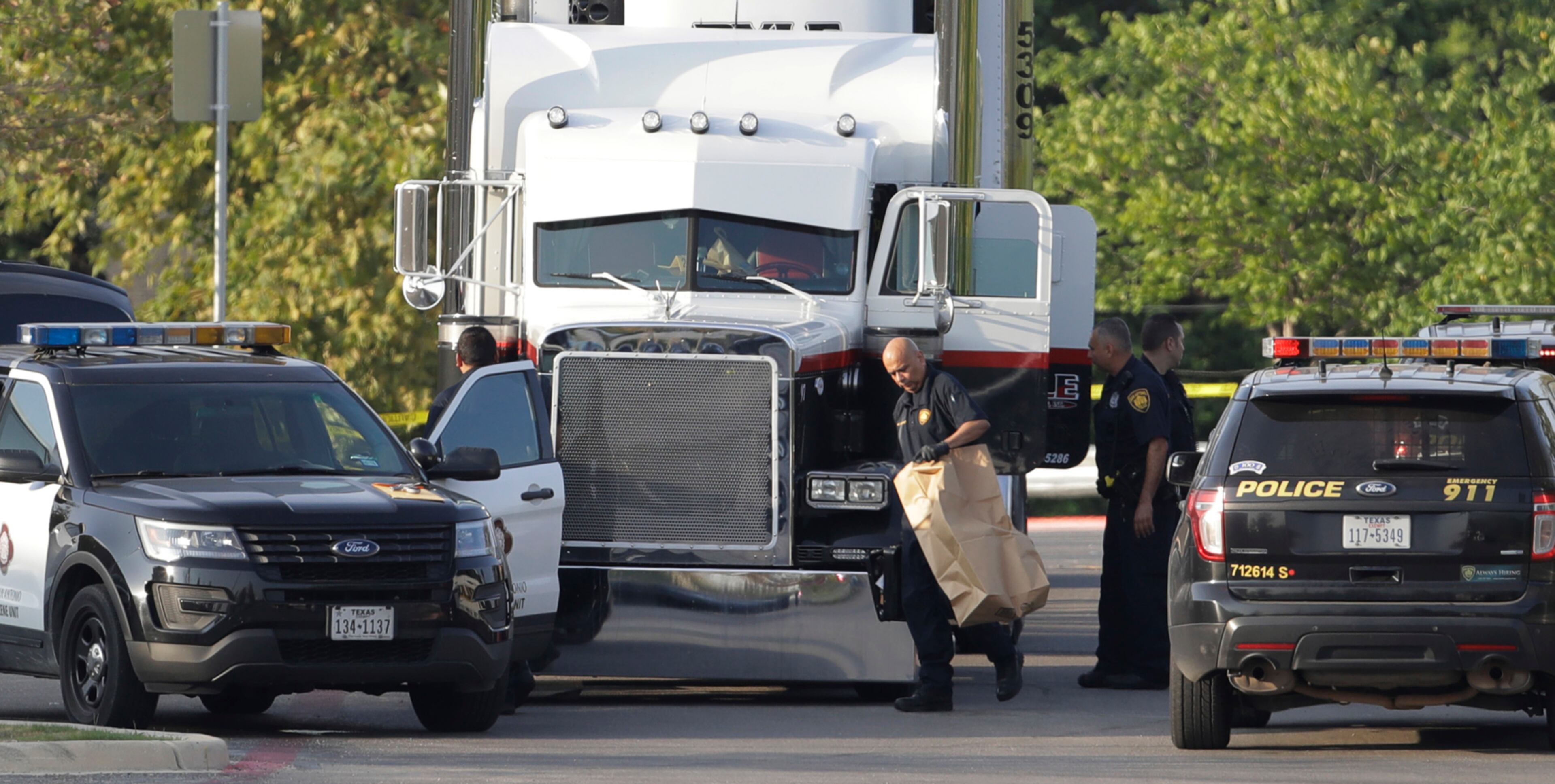 San Antonio police officers investigate the scene where eight people were found dead in a tractor-trailer loaded with at least 30 others outside a Walmart store in stifling summer heat in what police are calling a horrific human trafficking case, Sunday, July 23, 2017, in San Antonio. (AP Photo/Eric Gay)