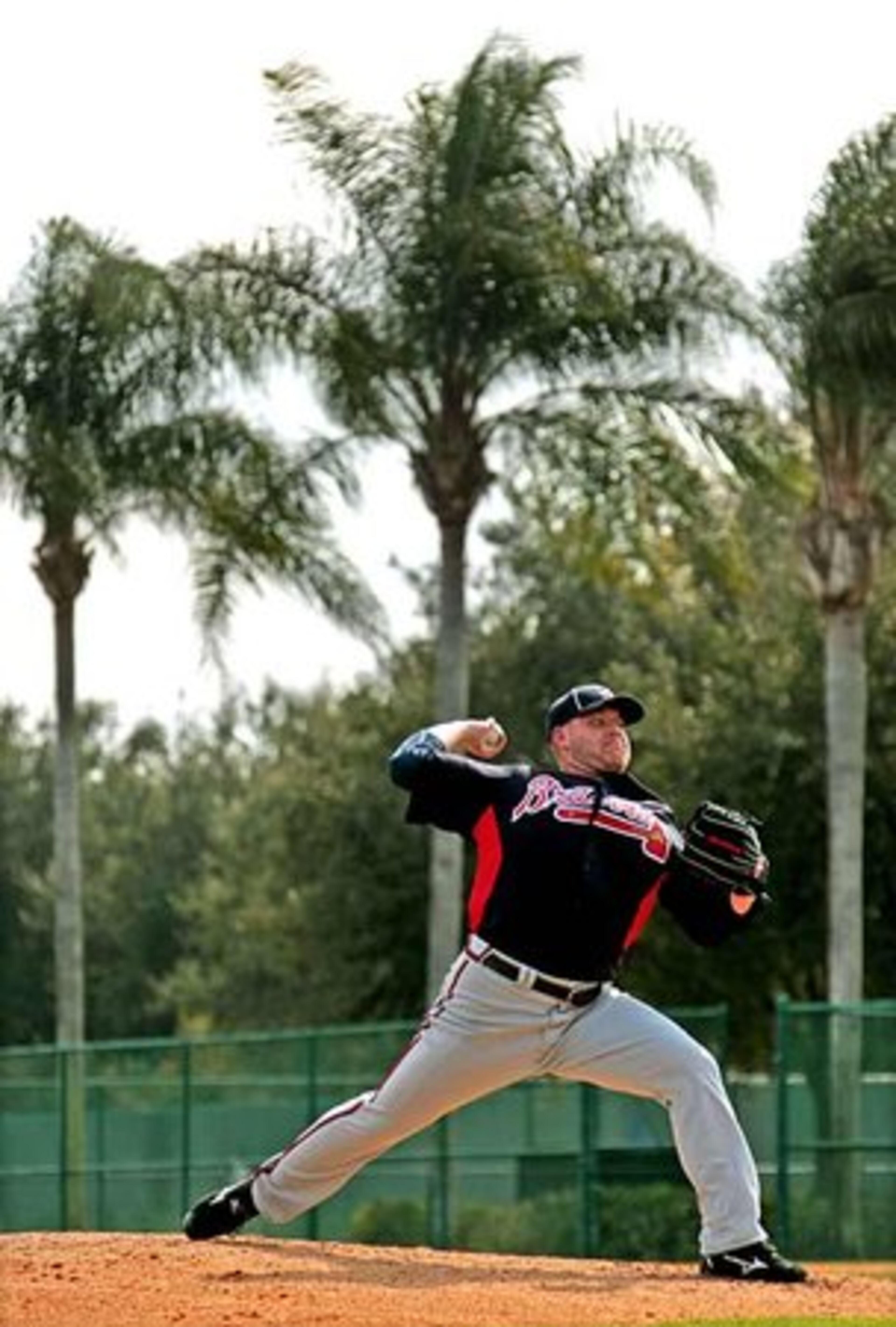 Braves pitcher Stephen Marek delivers to the plate below a line of palm trees.
