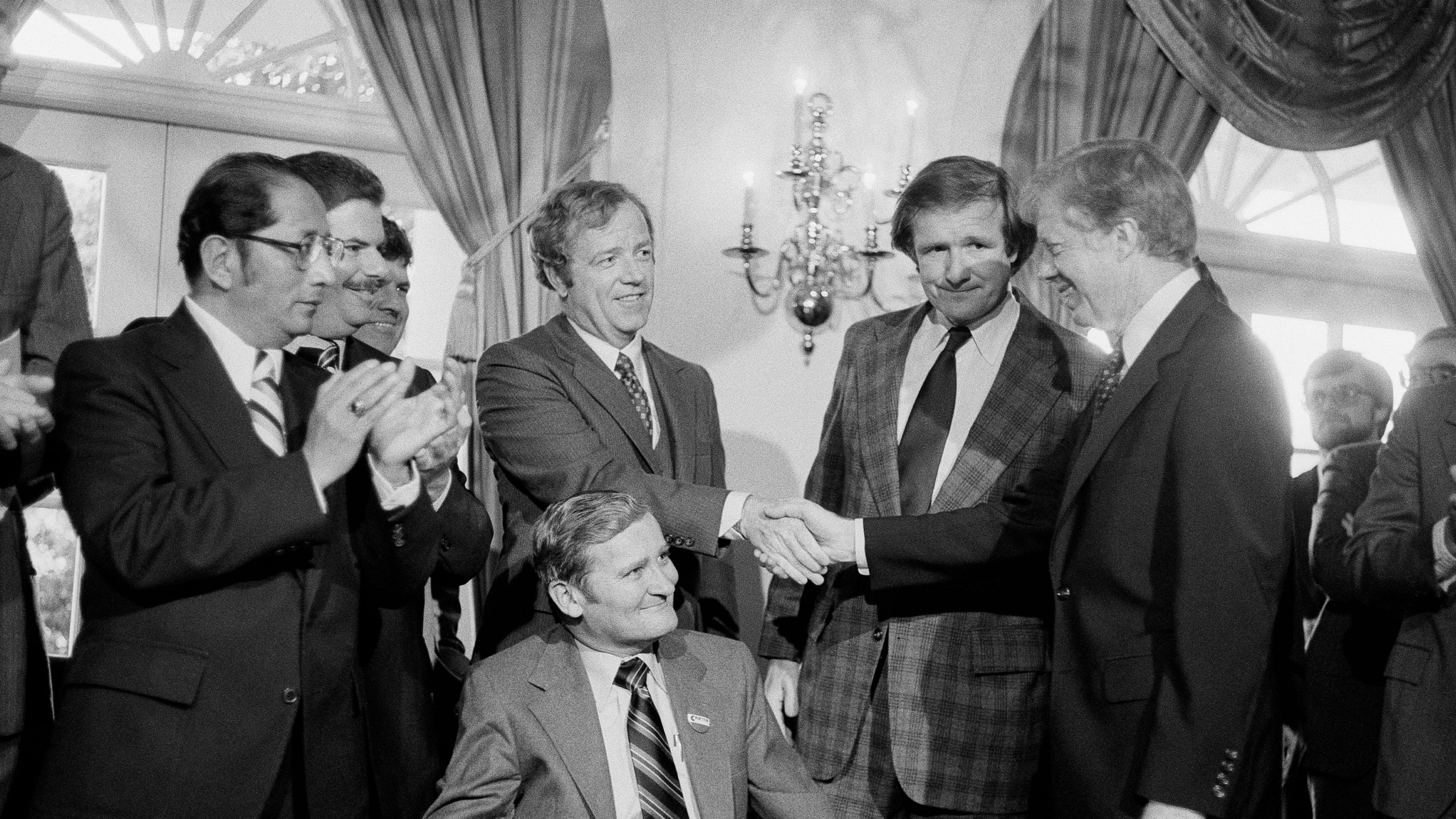 FILE - President Jimmy Carter, right, shakes hands with the Michigan delegation, in Washington, April 24, 1980, who were present for the signing by Carter of a bill that would enable Volkswagen to operate an auto assembly plant in a Detroit suburb. Sen. Don Riegle, D-Mich., next to Carter, and Michigan Senate Majority Leader William Faust seated center, look on. (AP Photo, File)