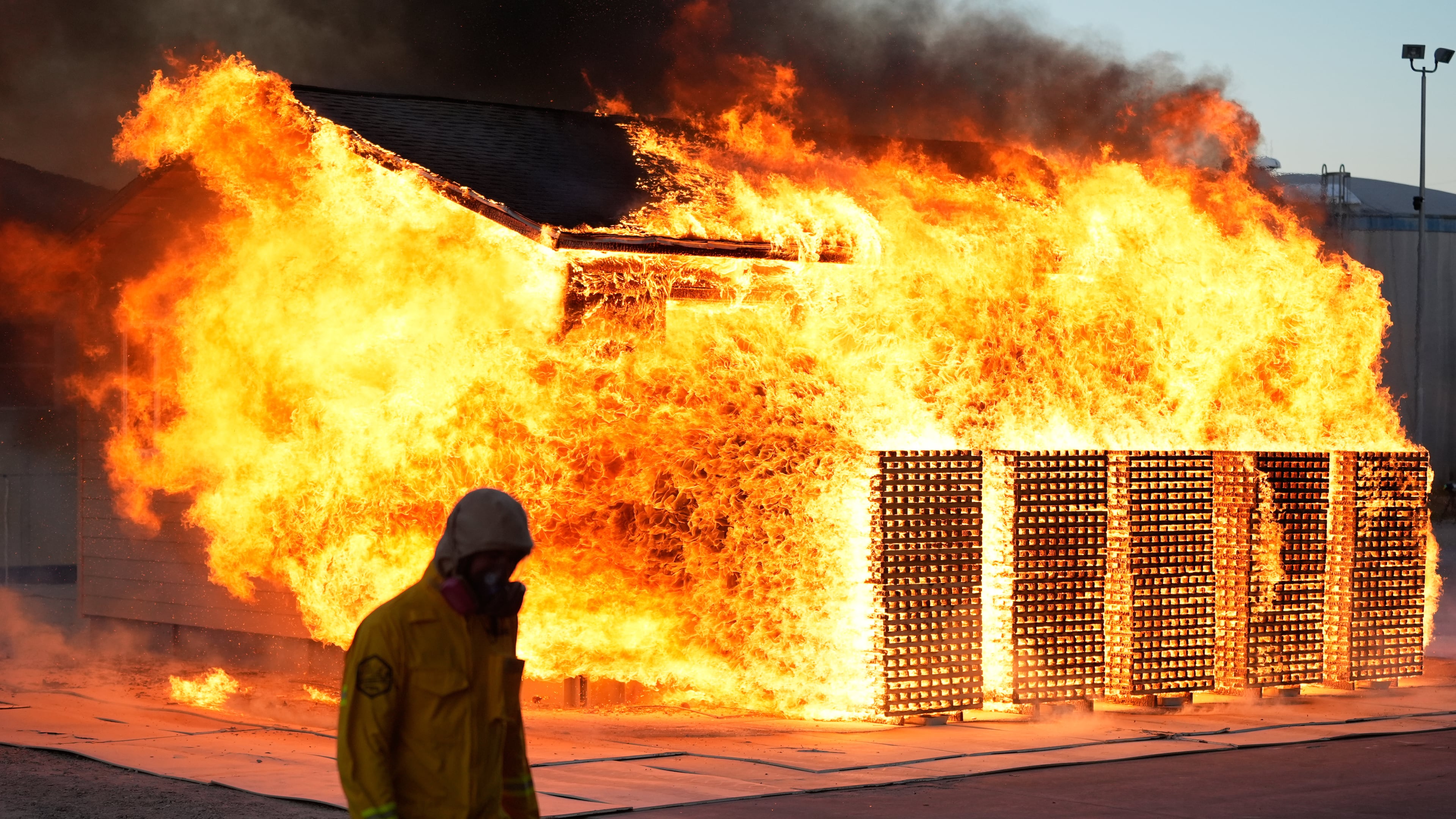 A wildfire researcher walks in front of an accessory dwelling unit burning during an experiment at the Institute for Business & Home Safety center on Thursday, April 16, 2026, in Richburg, S.C. (AP Photo/Erik Verduzco)