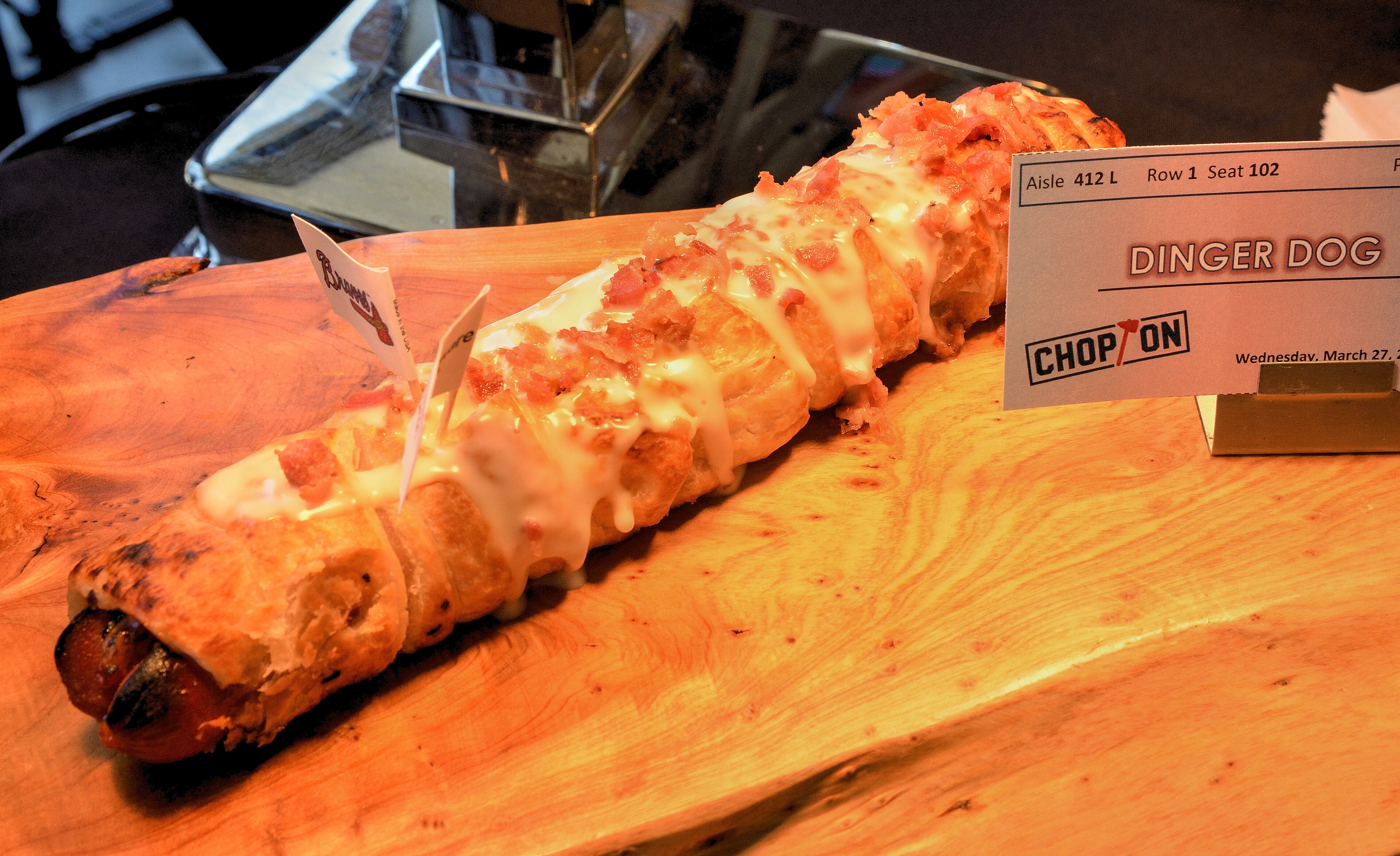 Dinger Dog (section 143). A footlong all-beef frank split and filled with bacon jam & cheddar cheese, wrapped in puff pastry and baked until golden brown. Topped with queso blanco and crispy bacon. $11.00