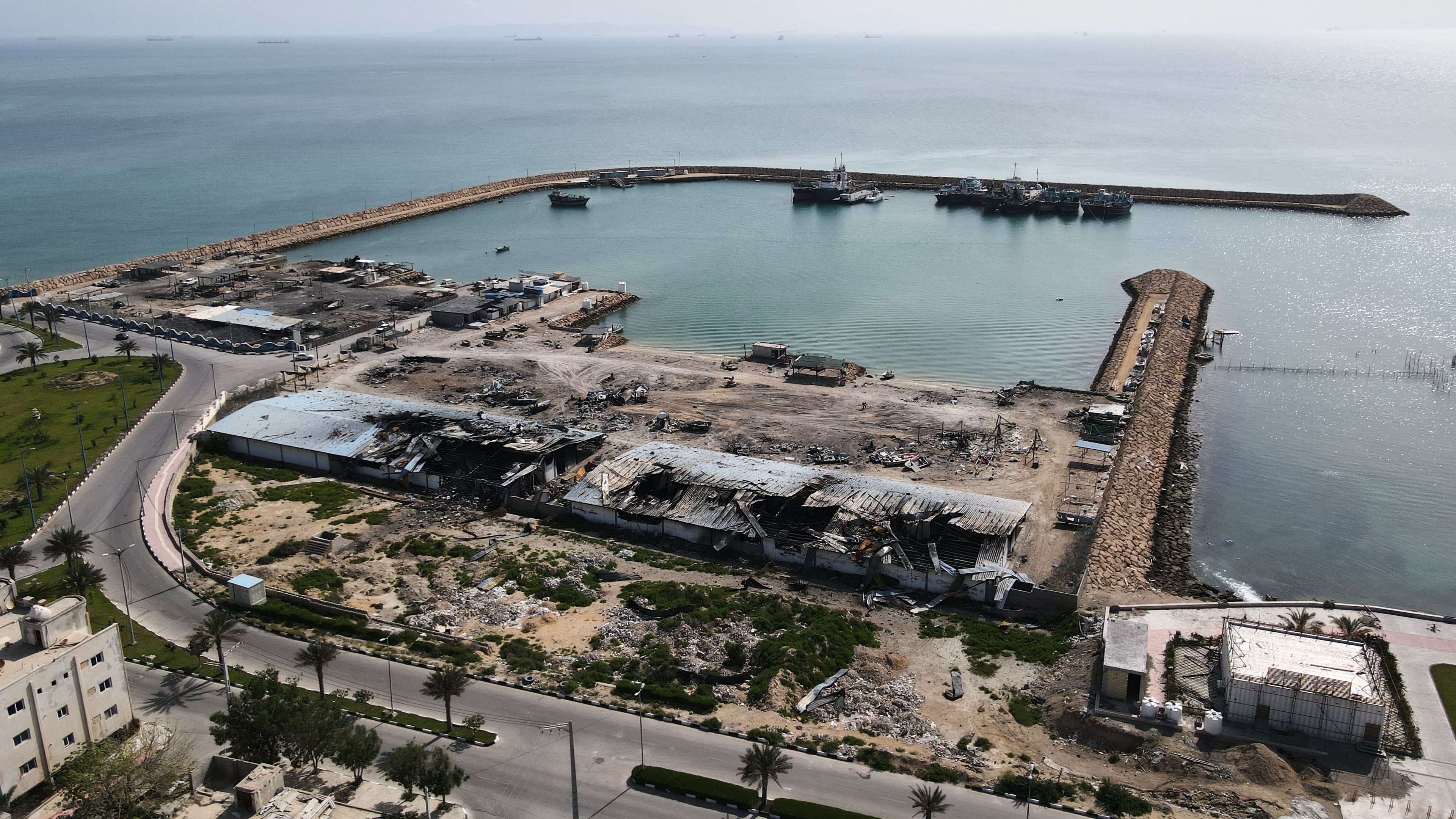 Backdropped by ships in the Strait of Hormuz, damage, according to local witnesses caused by several recent airstrikes during the U.S.-Israel military campaign, is seen on a fishing pier in the port of Qeshm island, Iran, Monday, April 13, 2026. (AP Photo/Asghar Besharati)