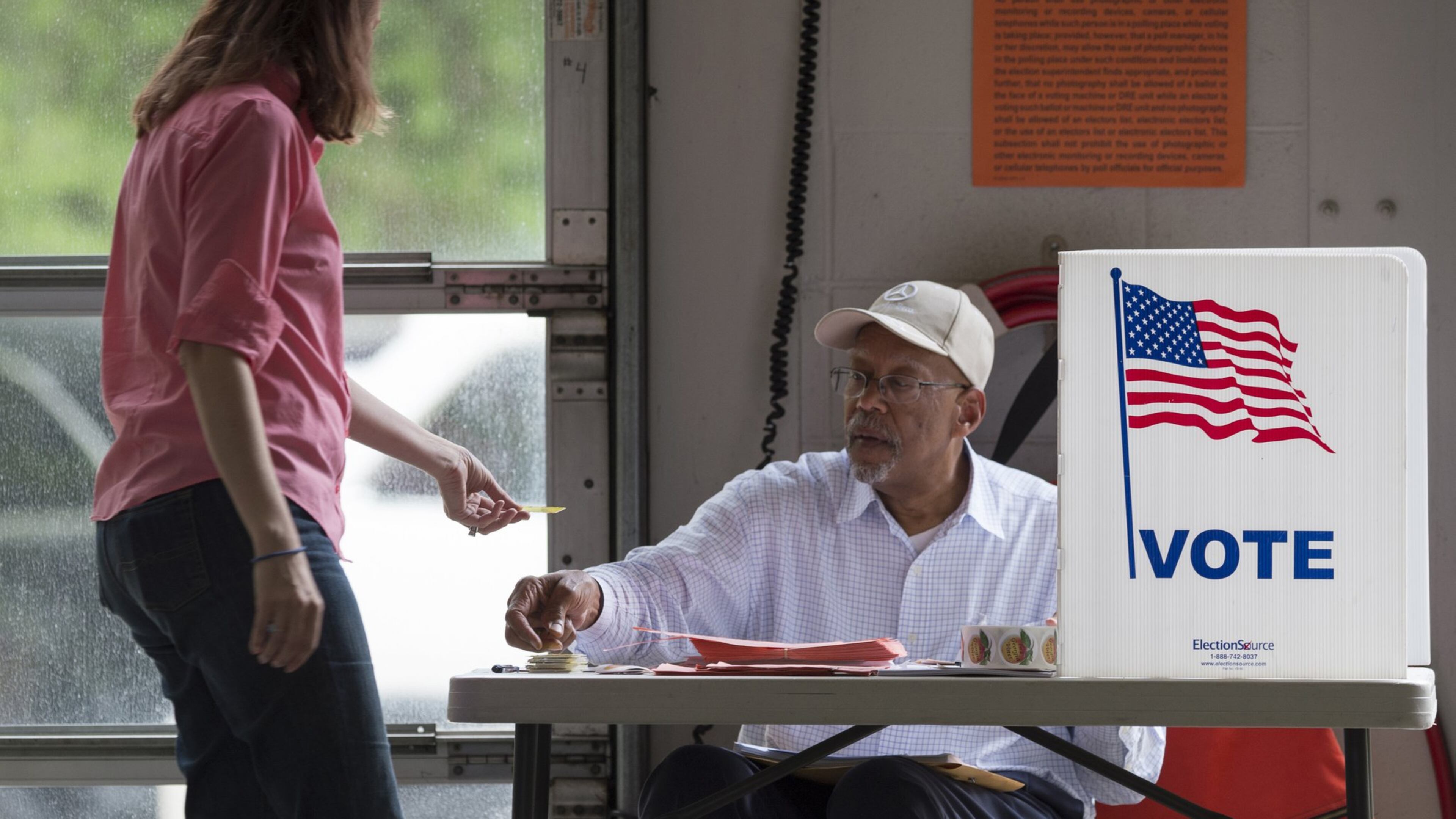 Toni Kuhn, left, hands her voter card to Birdel Jackson III at Alpharetta Fire Station 82 during an election in April. (DAVID BARNES / DAVID.BARNES@AJC.COM)