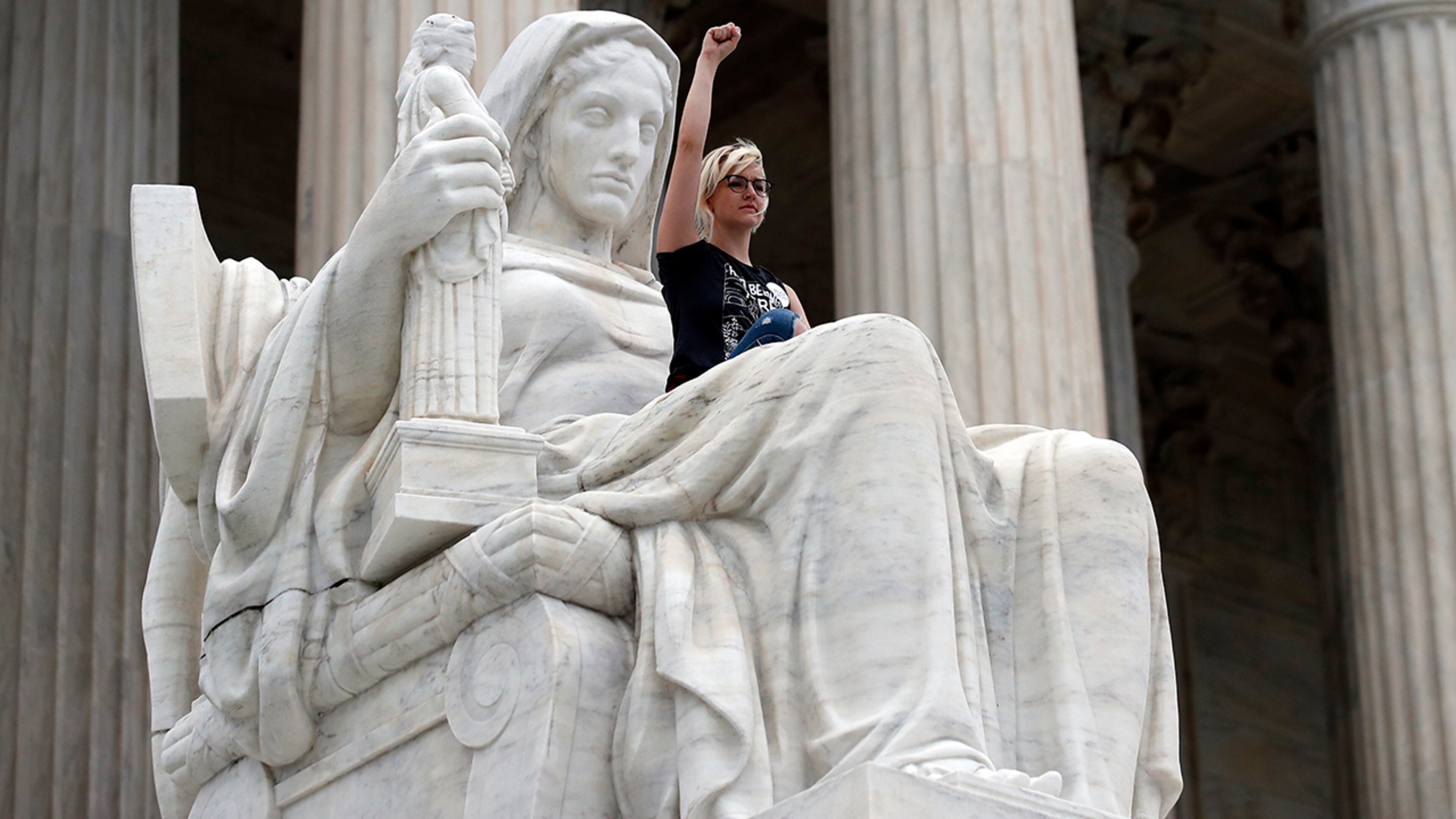 Jessica Campbell-Swanson, from Denver, sits in the lap of the Contemplation of Justice statue as activists protest on the steps of the Supreme Court after the confirmation vote of Supreme Court nominee Brett Kavanaugh, on Capitol Hill, Saturday, Oct. 6, 2018 in Washington. (AP Photo/Alex Brandon)