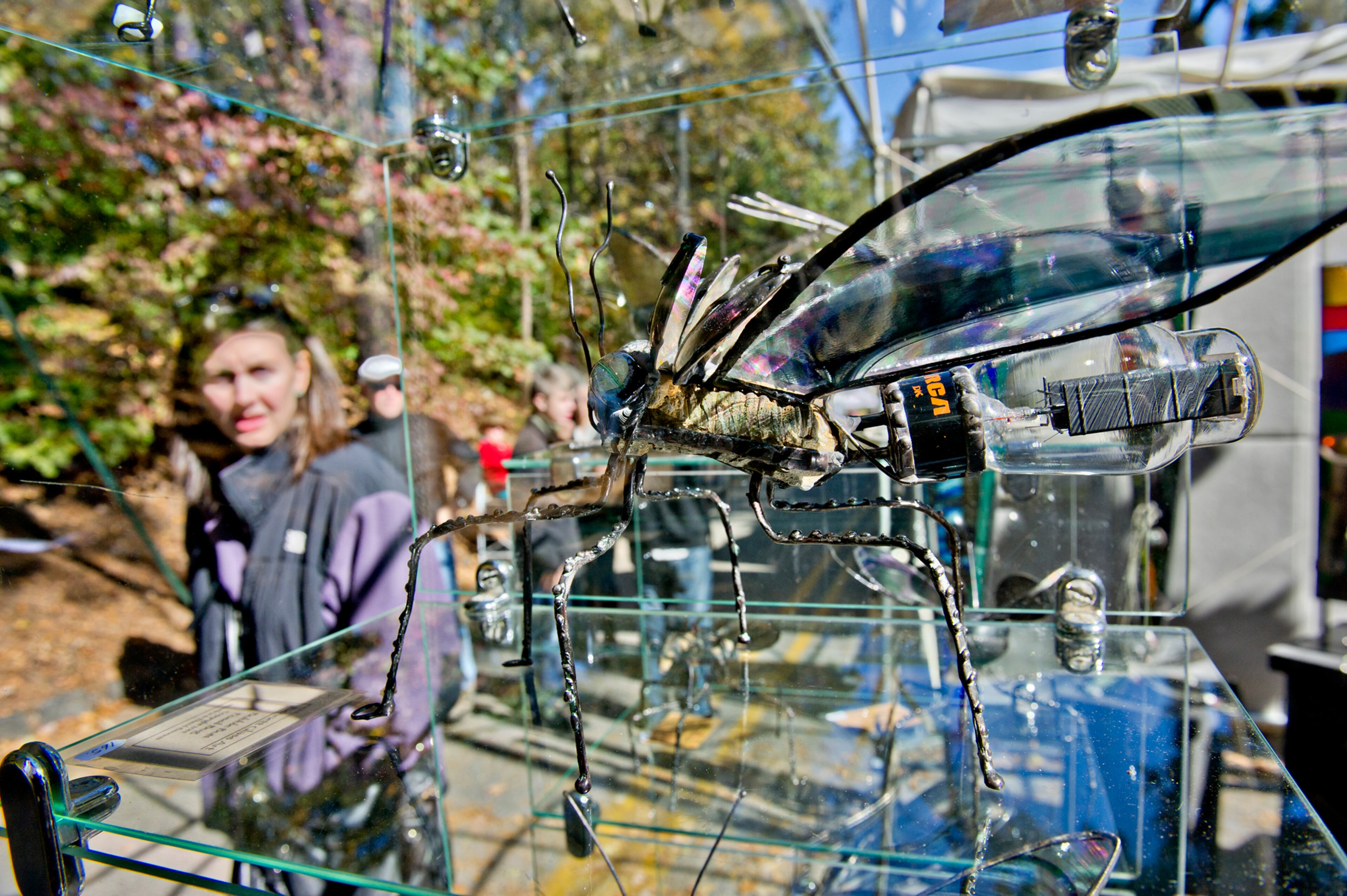 A glass and found object bug sculpture sits on display in Veronica and David Bennet's booth as Erin Rogan passes by during the Chastain Park Art Festival in Atlanta on Sunday, November 2, 2014. Although cold temperatures kept attendance down on Saturday, the sun on Sunday brought out thousands of people to check out art by local, regional and national artists. JONATHAN PHILLIPS / SPECIAL