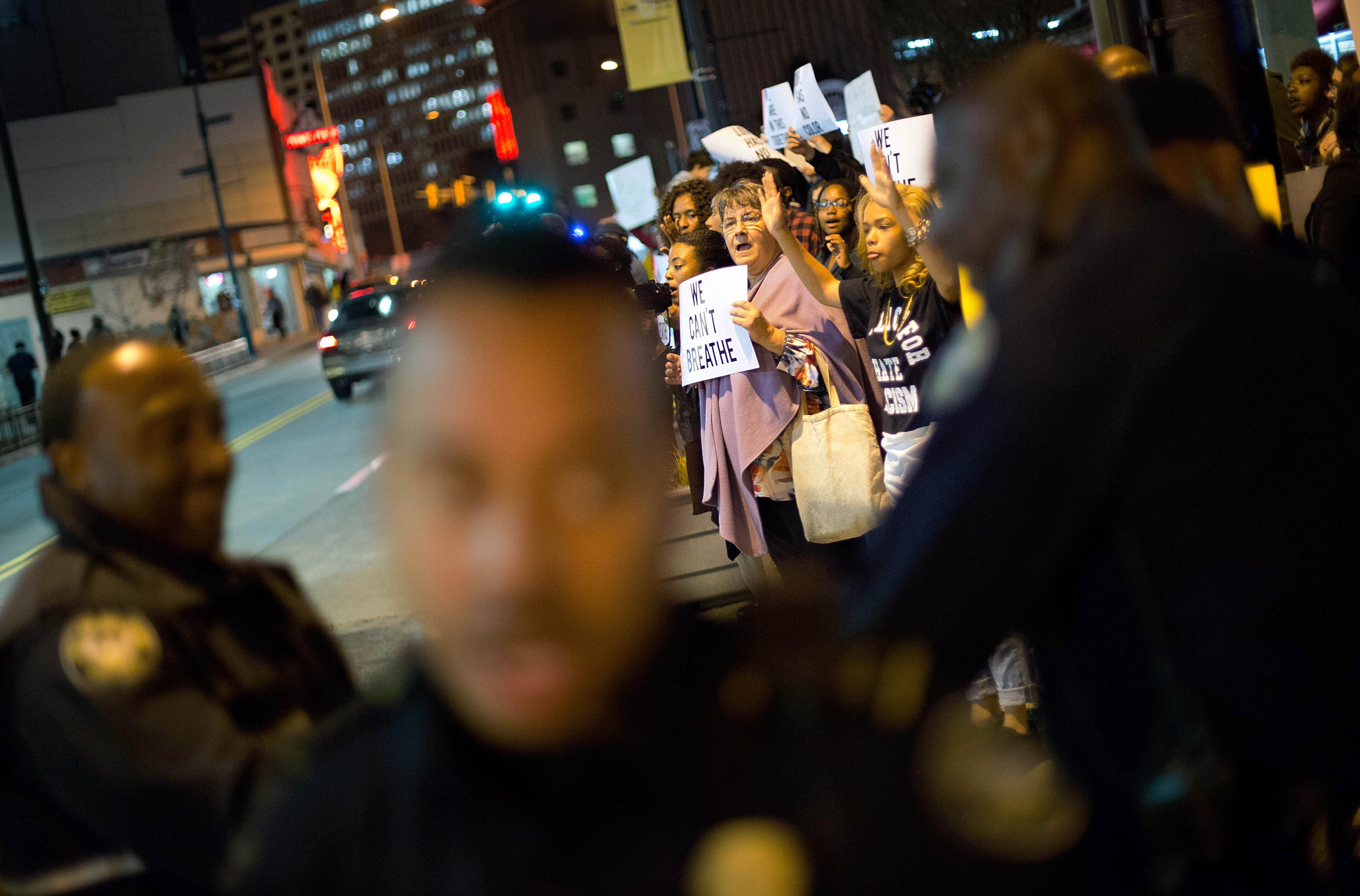 Police stand on a street corner as protesters demonstrate in Atlanta on Thursday, Dec. 4, 2014 against the deaths of two unarmed black men at the hands of white police officers in New York City and Ferguson, Mo. (AP Photo/David Goldman)