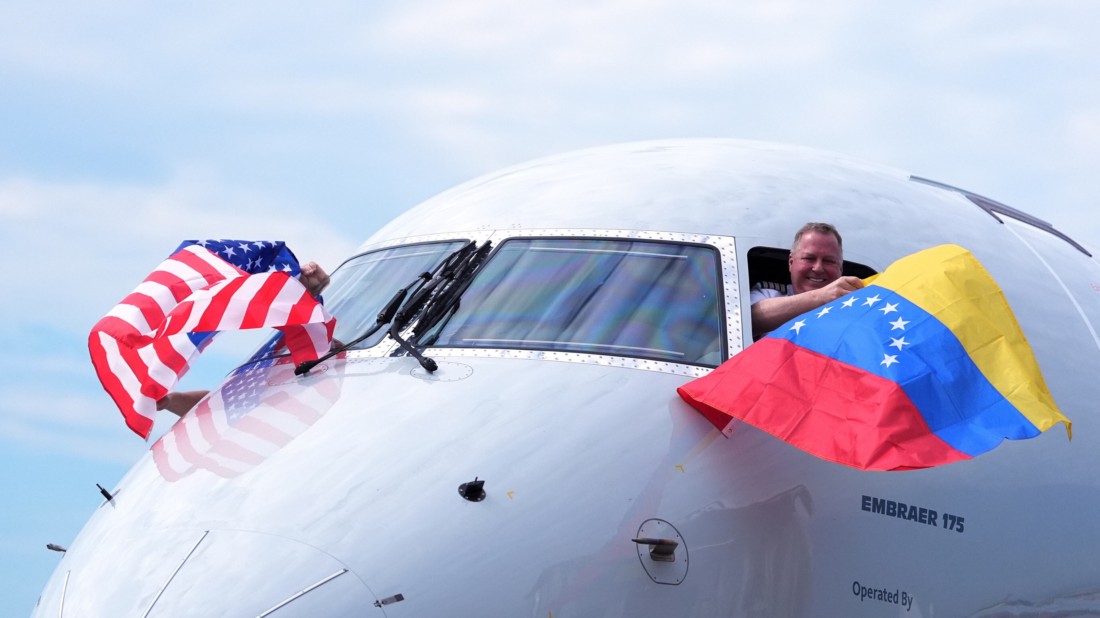 Capt. Ric Wilson waves a Venezuelan flag and the first officer waves a U.S. flag as they prepare to fly American Airlines Flight AA3599, the first direct commercial flight between the United States and Venezuela in seven years, Thursday, April 30, 2026, at Miami International Airport in Miami. (AP Photo/Rebecca Blackwell)