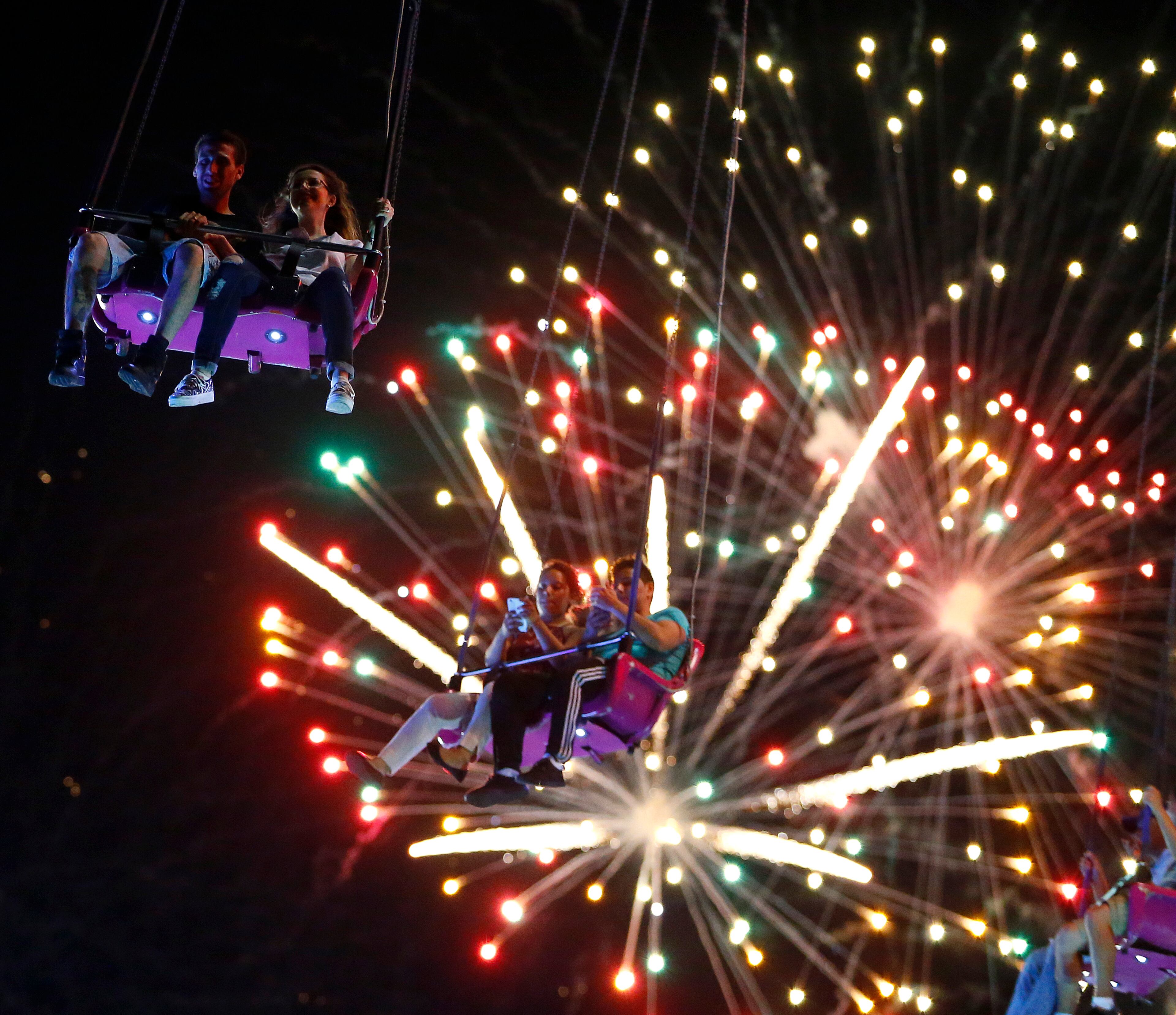People ride the Sky Flyer at State Fair Meadowlands carnival as fireworks explode, Sunday, July 3, 2016, in East Rutherford, N.J. (AP Photo/Julio Cortez)