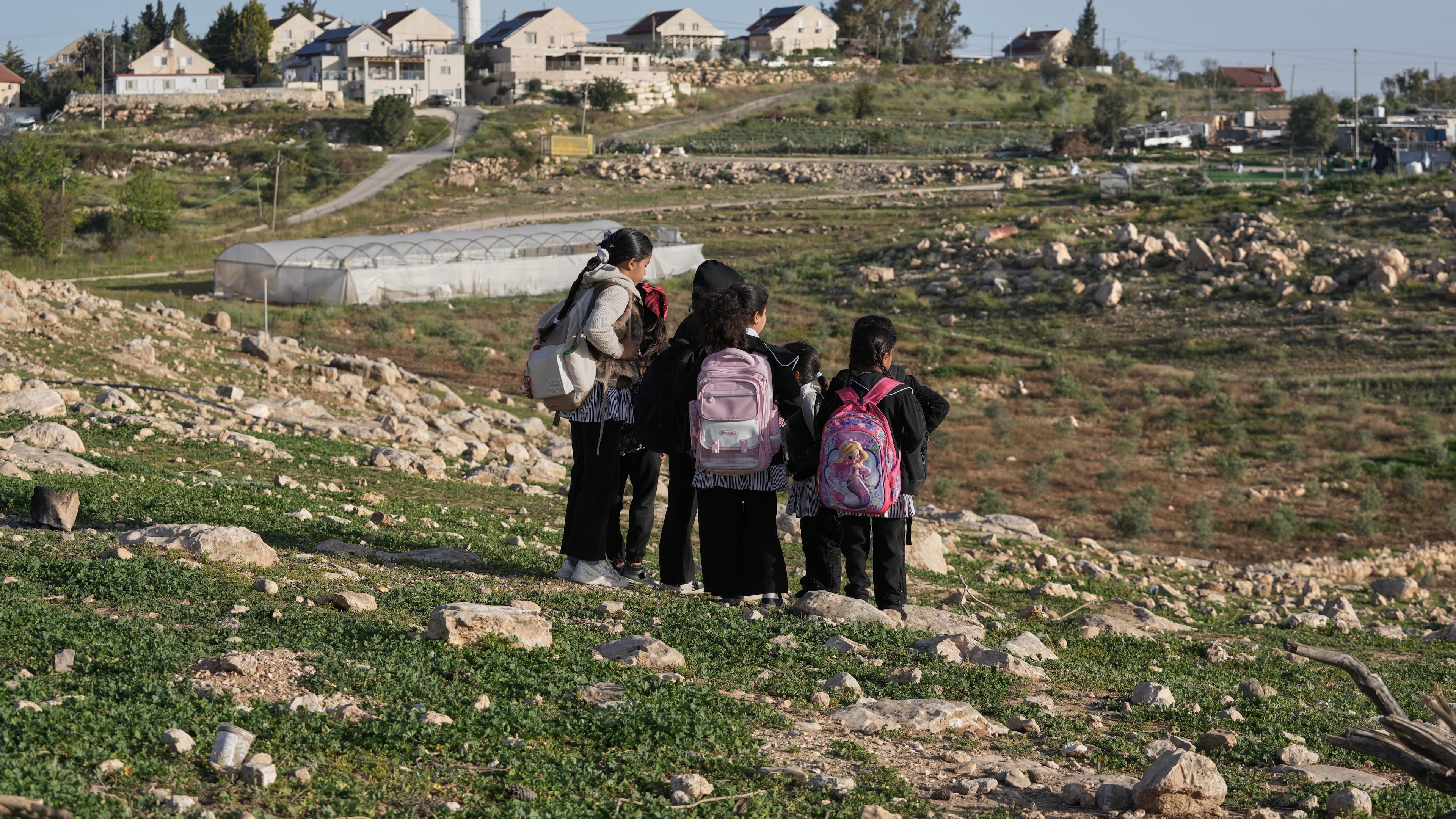 Palestinian students walk to school using an alternative route that is nearly twice as long because a fence separates their village from the nearby Israeli settlement of Carmel, near the West Bank village of Umm al-Khair, Tuesday, April 14, 2026. (AP Photo/Mahmoud Illean)