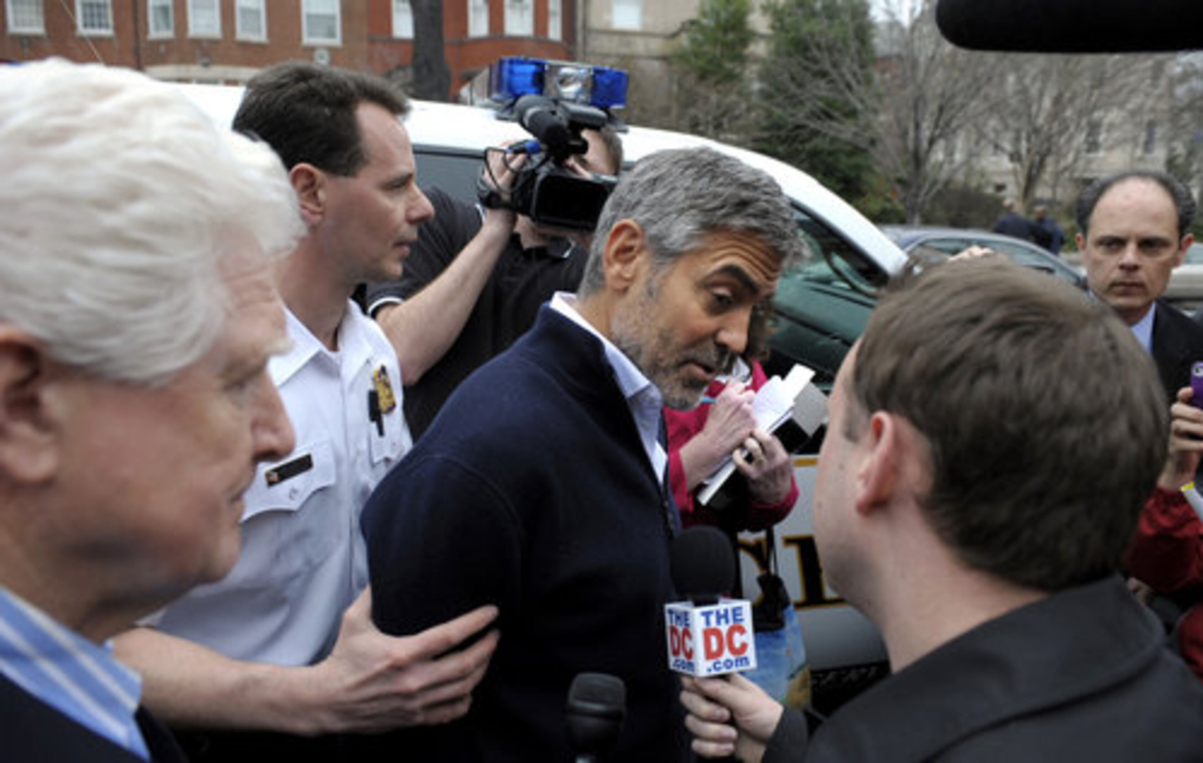 George Clooney speaks to the media as he is led to a police vehicle after being arrested.