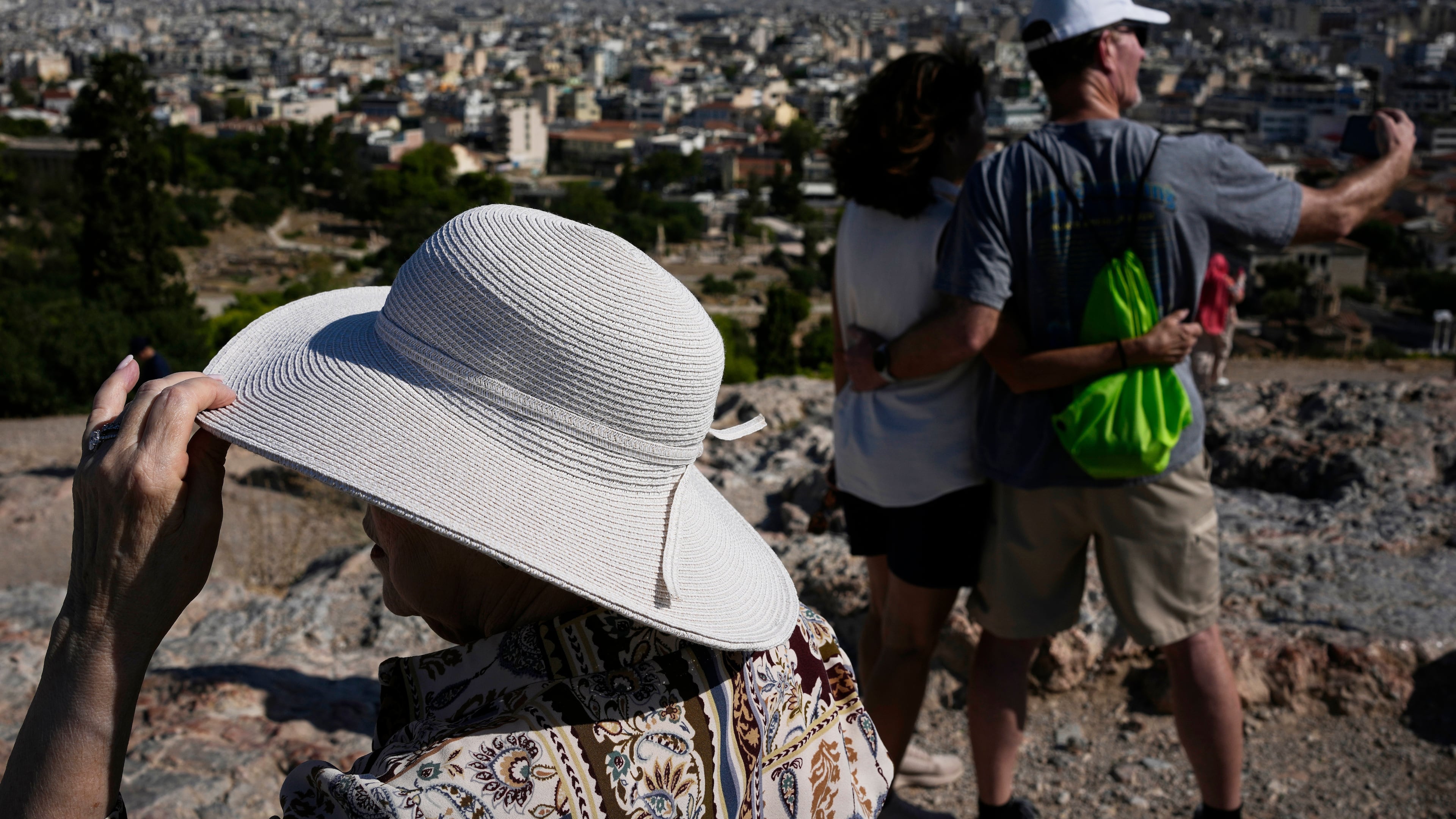 Tourists wearing hats take photographs on the rocky Areios Pagos Hill next to the Acropolis in Athens, Greece, Friday, Aug. 14, 2026. (AP Photo/Thanassis Stavrakis)