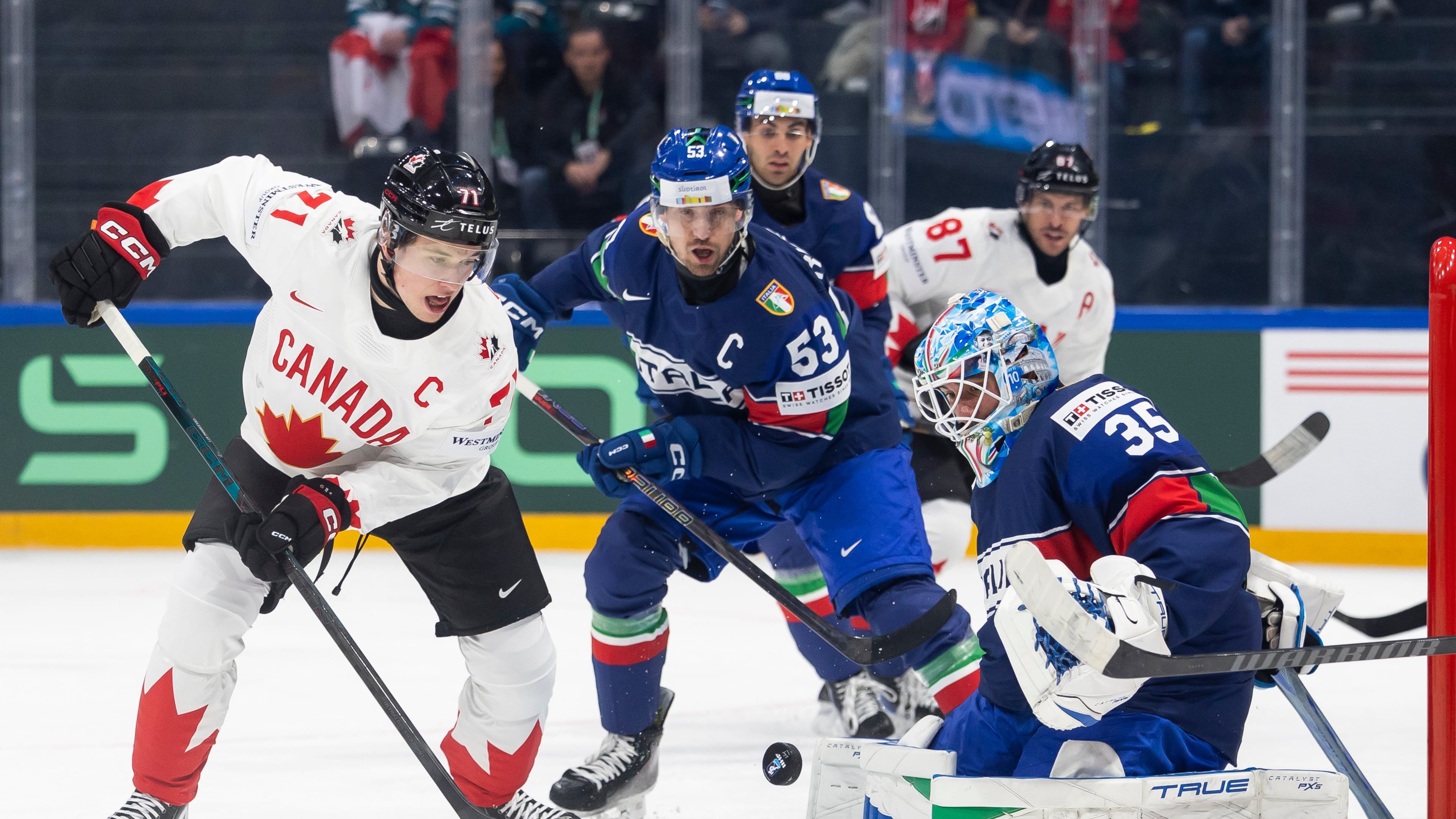 Canada's Macklin Celebrini, left, vies for the puck against Italy's Alex Trivellato, center, and Italy's goaltender Davide Fadani, right, during the 2026 IIHF Men's Ice Hockey World Championship preliminary round group B game between Italy and Canada, in Fribourg, Switzerland, Saturday, May 16, 2026. (Cyril Zingaro/Keystone via AP)
