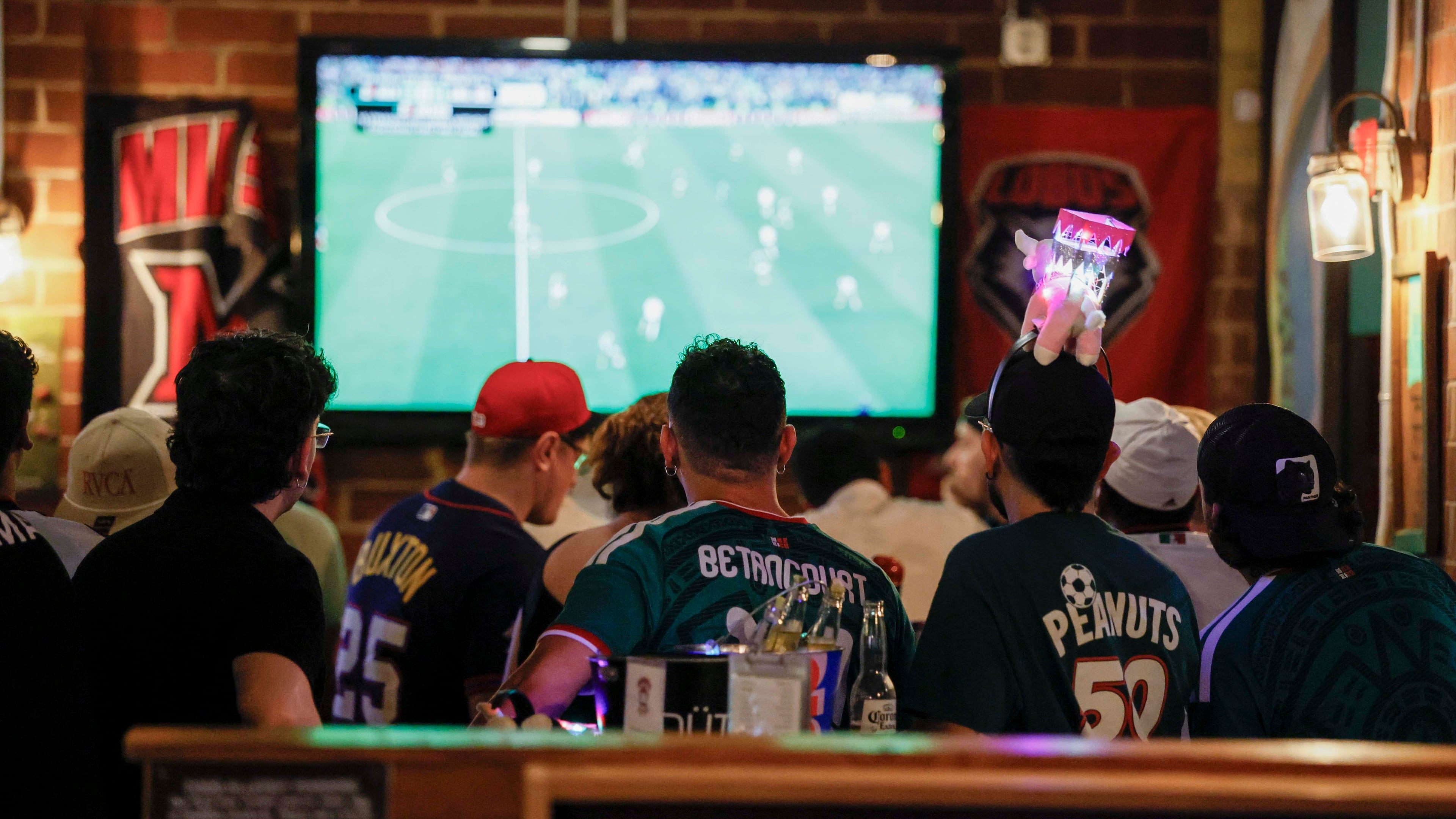 A group of customers, some wearing Mexico jerseys, watch a World Cup game on screens at Woofs Sport Bar in Midtown on Sunday, July 5, 2026. Woofs is the official location for Pride House ATL, the city’s designated hub for LGBTQ+ soccer fans during the FIFA World Cup. (Miguel Martinez/AJC)