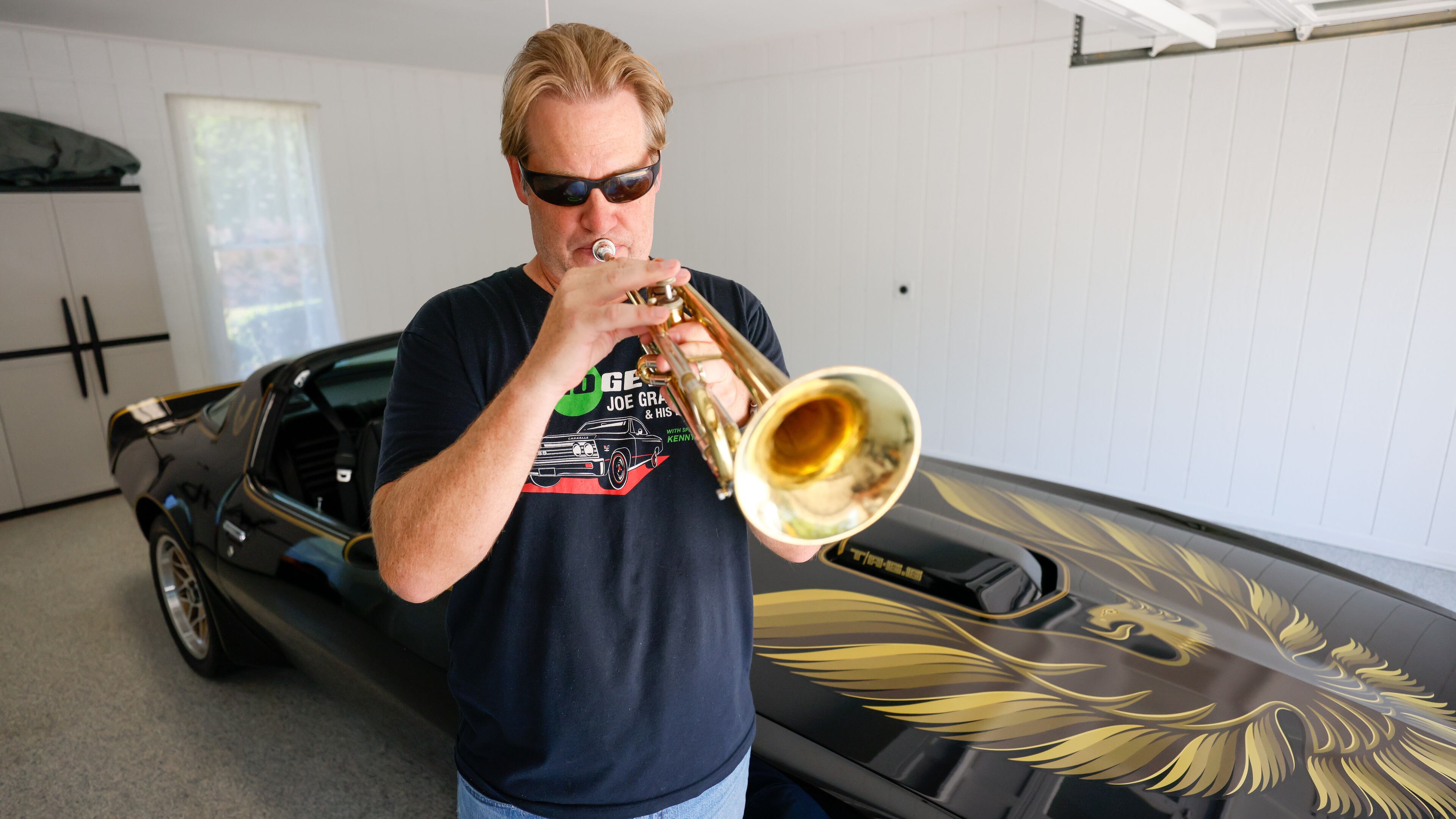 Musician Joe Gransden plays his trumpet next to his meticulously restored 1979 Pontiac Trans Am in his home’s garage.
(Miguel Martinez / AJC)