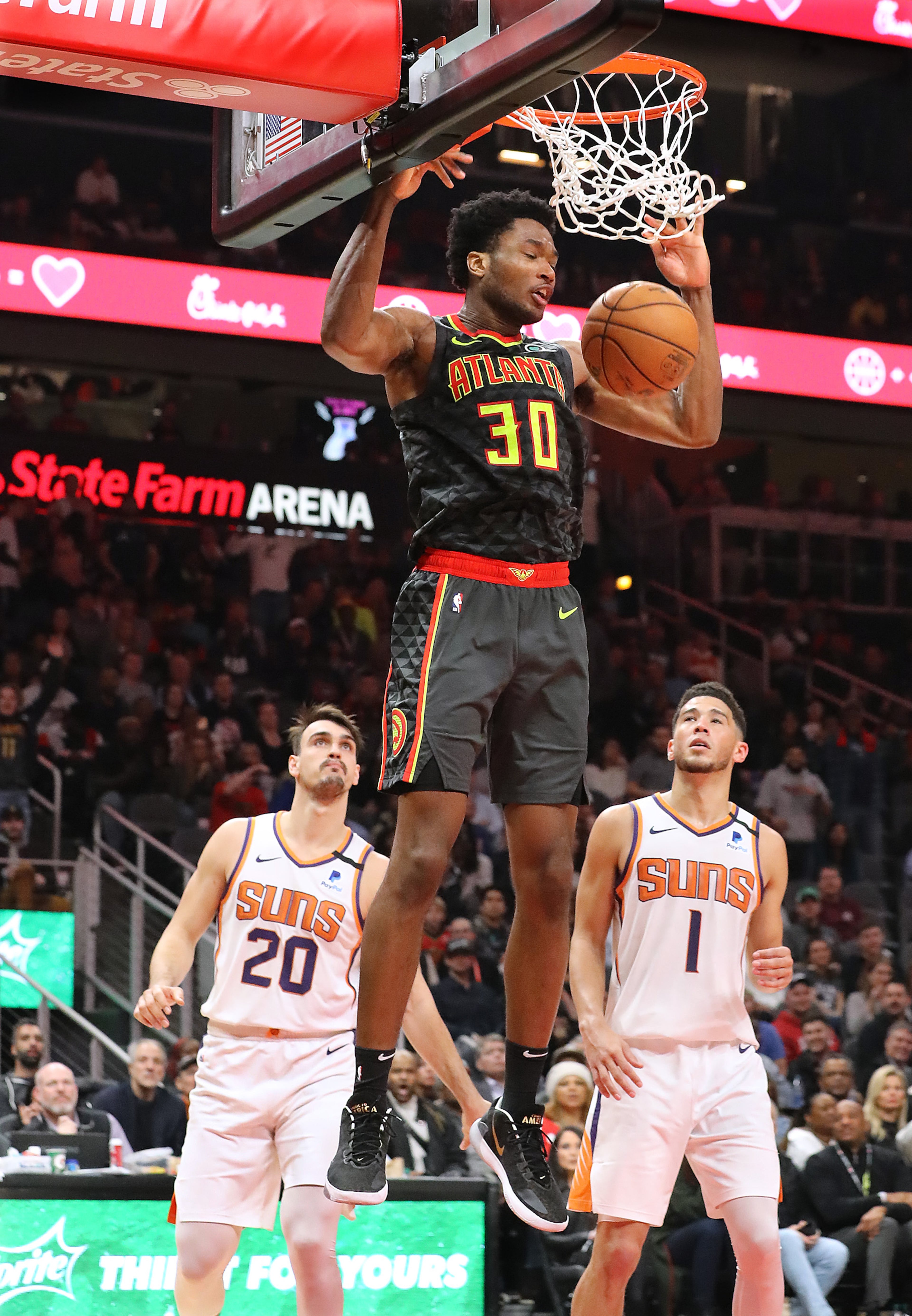 Hawks center Damian Jones slams for two over Phoenix Suns defenders Dario Saric (left) and Devin Booker during a 123-110 victory in a NBA basketball game on Tuesday, January 14, 2020, in Atlanta. Curtis Compton ccompton@ajc.com