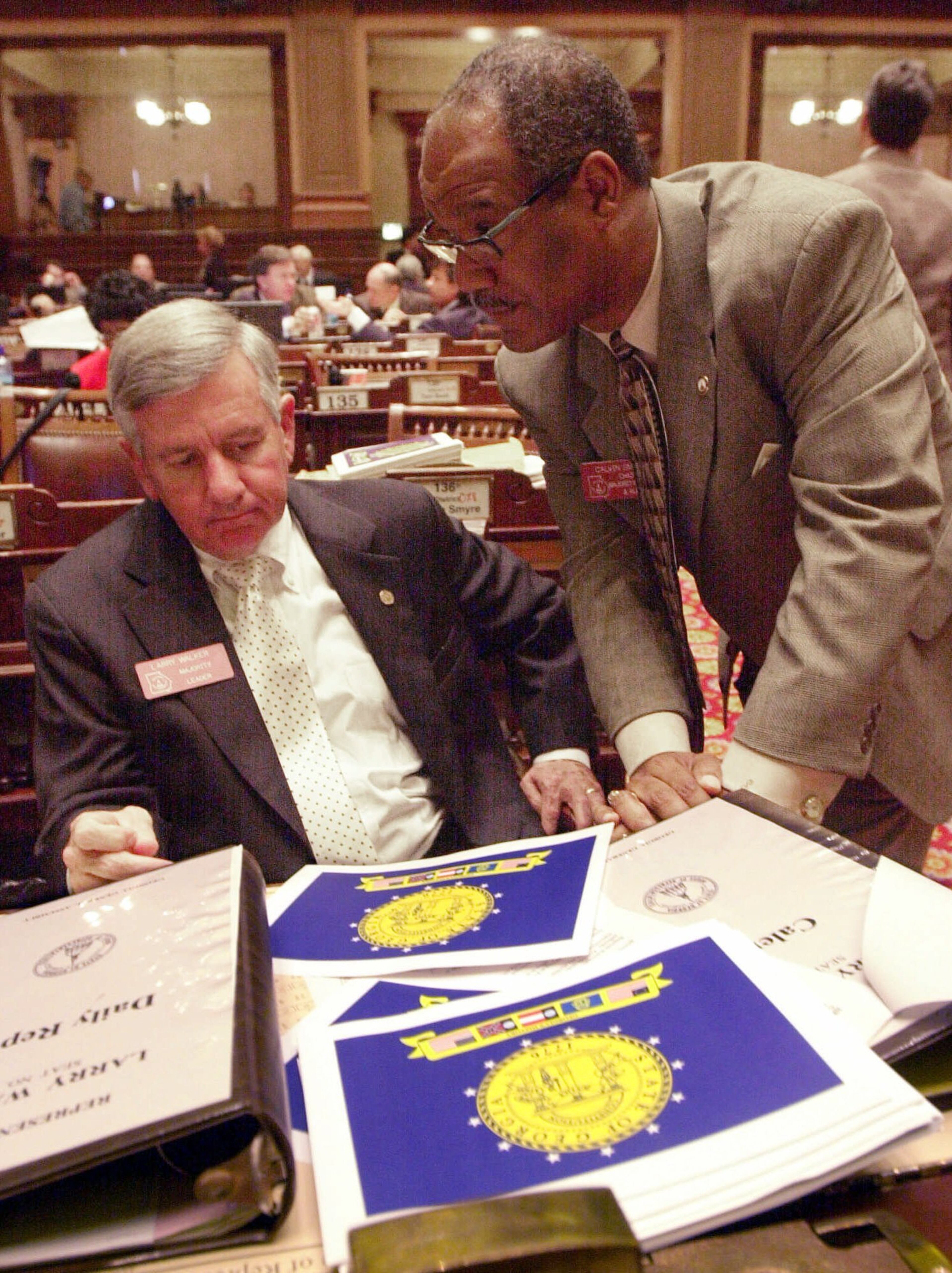 Prints showing the proposed new Georgia state flag line the desk of House Majority Leader Rep. Larry Walker, D-Perry, left, on the floor of the House in Atlanta as he talks with Rep. Calvin Smyre, D-Columbus, right, about the bill that would adopt the depicted flag Wednesday, Jan. 24, 2001. (AP Photo/Ric Feld