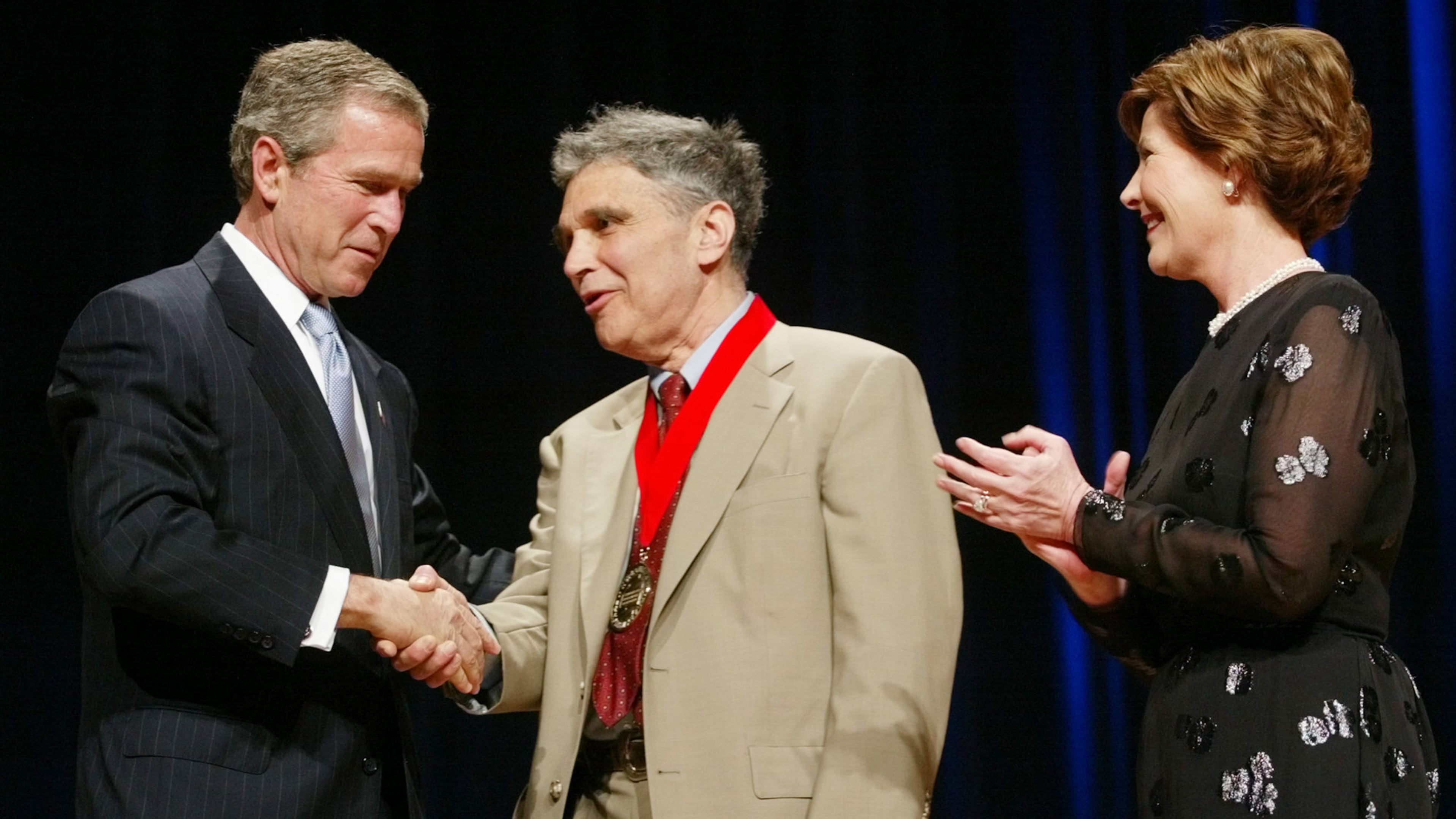 FILE - President Bush, left, shakes hands with Robert Coles, center, a child psychologist, researcher and professor of psychiatry from Cambridge, Mass., as first lady Laura Bush looks on during the National Endowment for the Arts Awards ceremony at Constitution Hall, April 22, 2002, in Washington. (AP Photo/Pablo Martinez Monsivais, File)