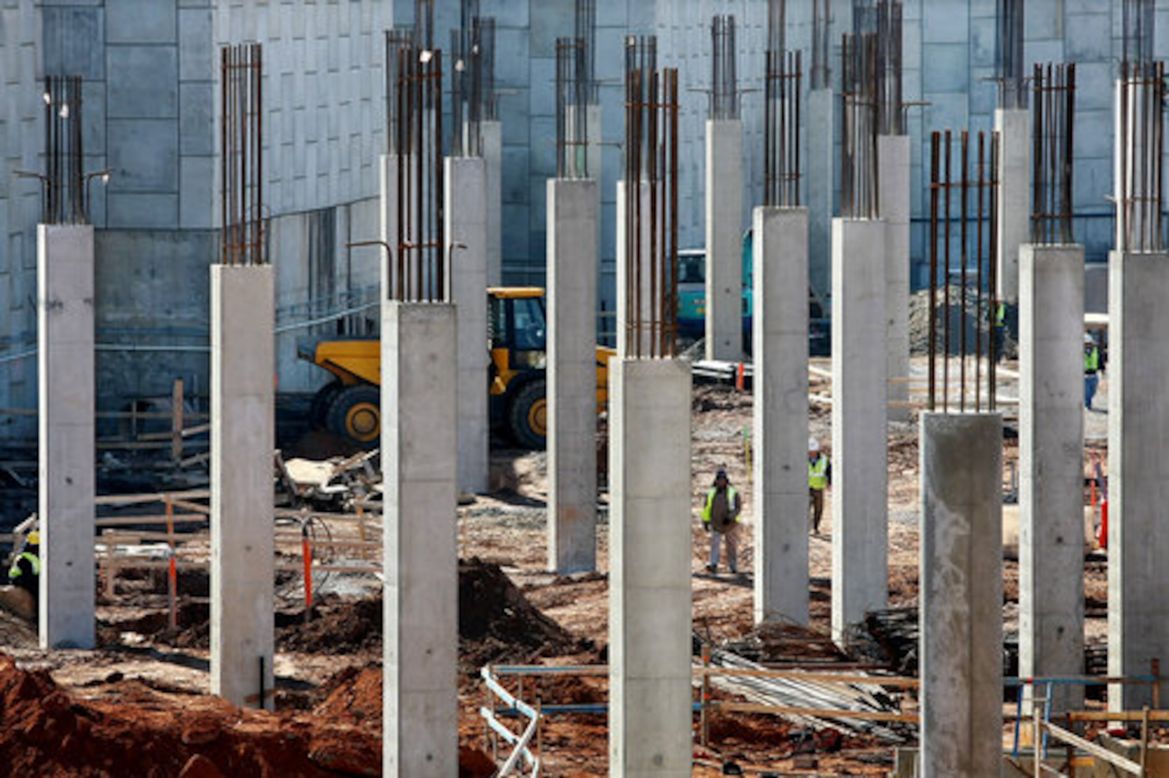 Construction workers are dwarfed by concrete support columns.