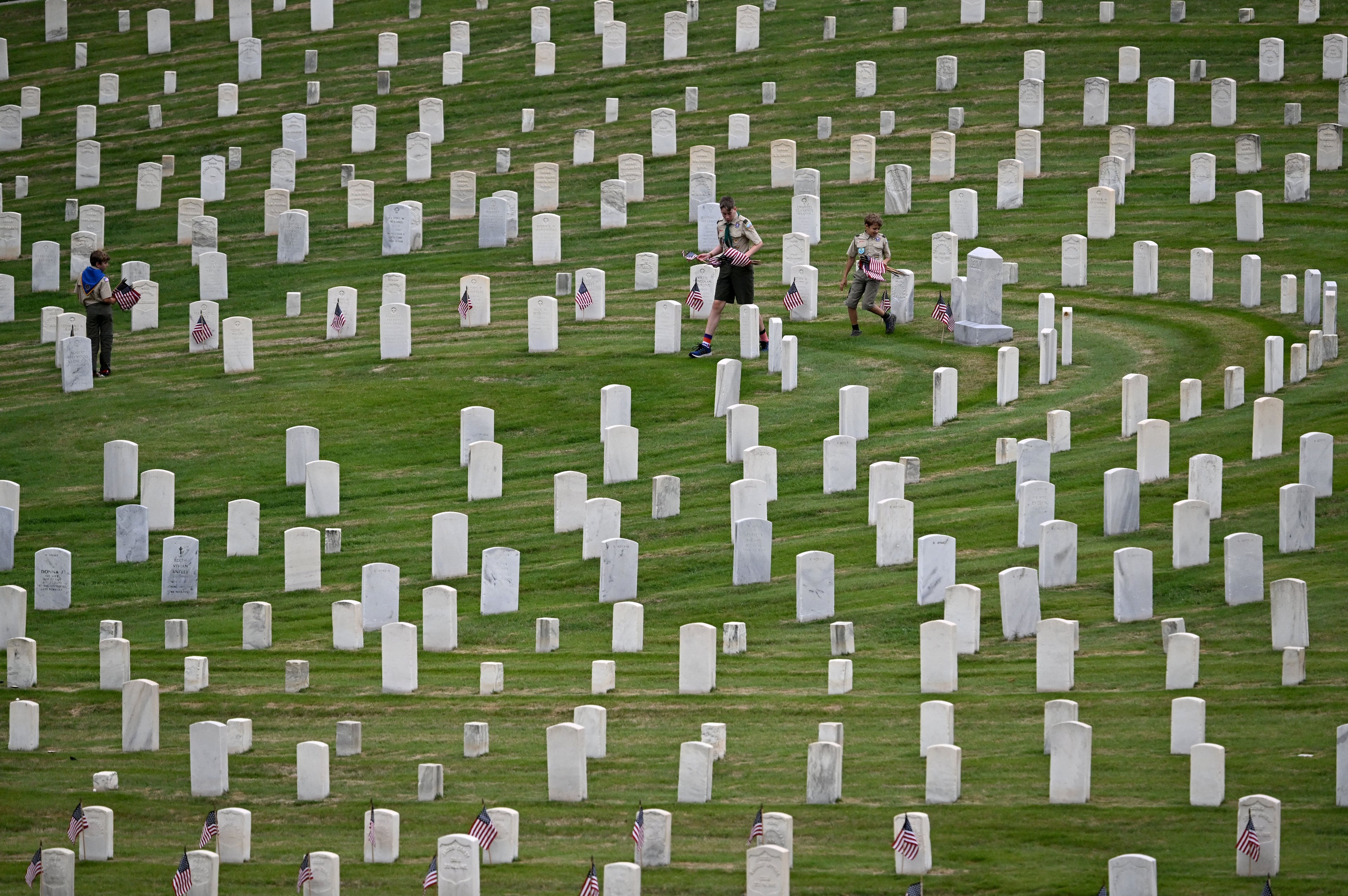 Scouts place a flag in front of a headstone during the Memorial Day Flag Placement event at Marietta National Cemetery on Saturday, May 23, 2026, in Marietta. Scouting groups in the community place more than 18,000 U.S. veteran grave flags at Marietta National Cemetery each year on the Saturday before Memorial Day, helping prepare for Monday’s ceremony. The long-running service project—organized with the National Memorial Day Association of Georgia—also gives youth and adults an opportunity to honor fallen service members and learn about their sacrifices and the area’s history. (Hyosub Shin/AJC)