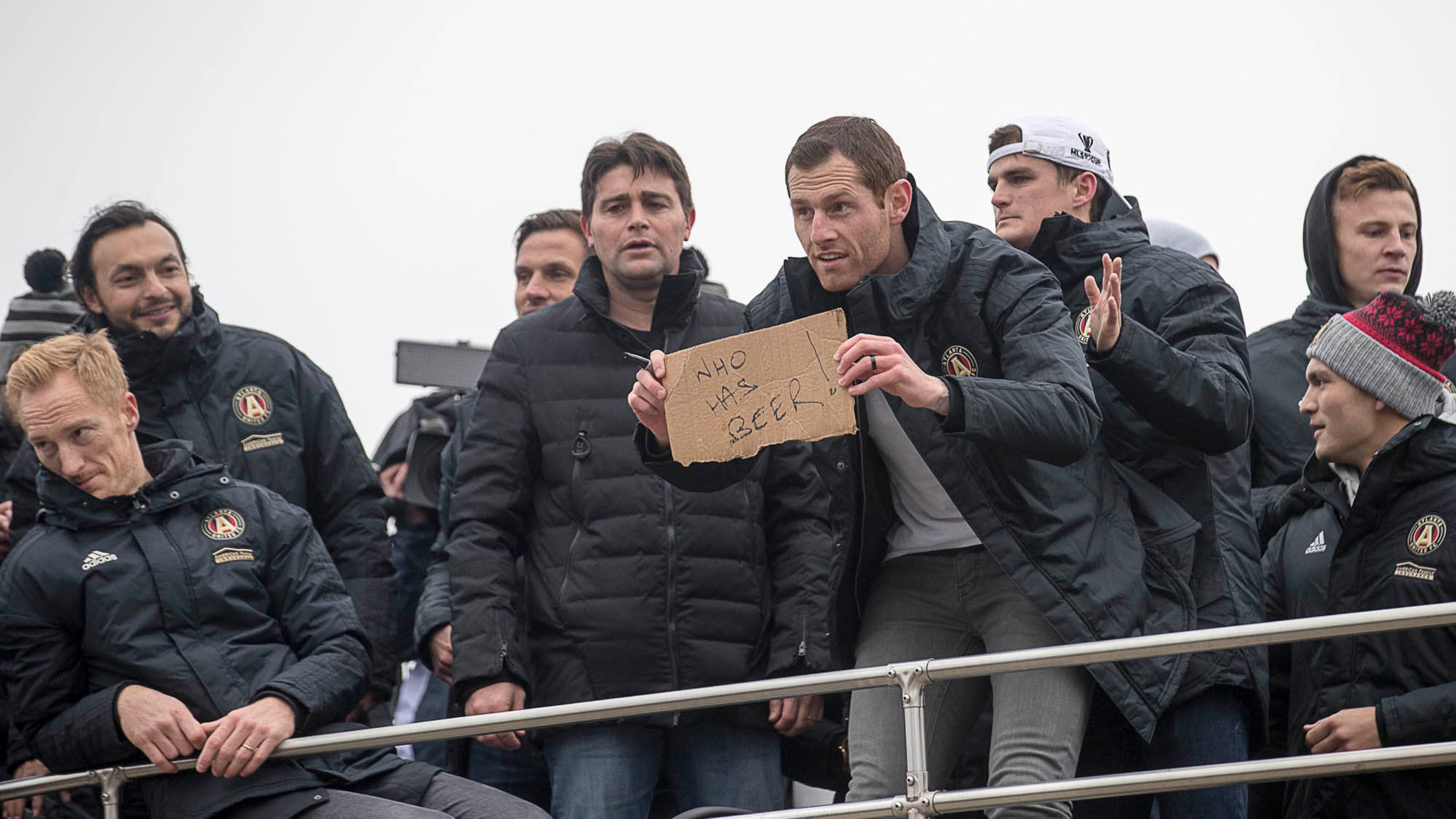 A member of Atlanta United's entourage asks fans for beer before the start of the victory rally from atop one of the double-decker buses carrying the MLS champions Monday, Dec. 10, 2018, during a parade through downtown Atlanta.