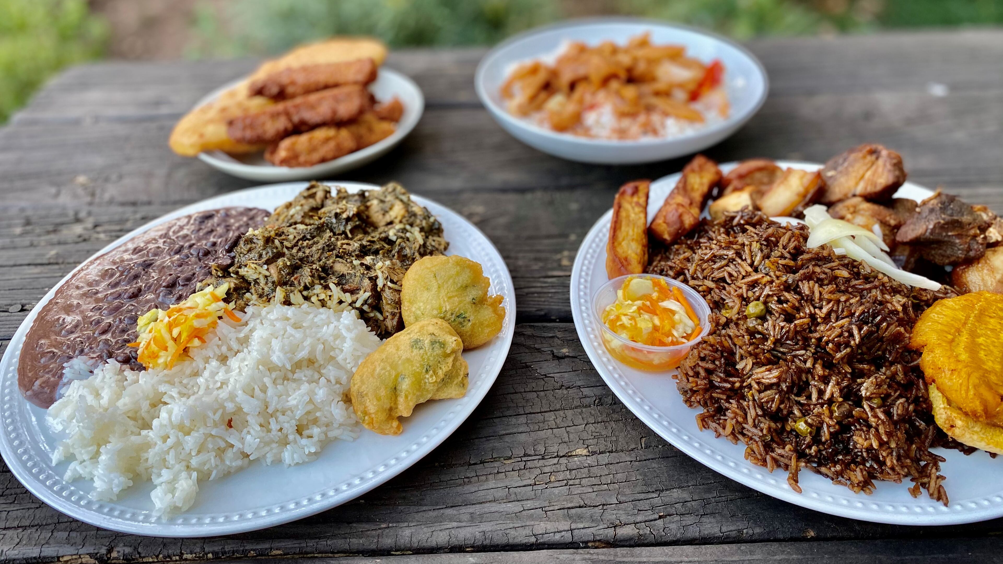 This takeout order from Jojo Fritay includes (left) lalo with white rice, black beans, pikliz and marinad; and (right) griot with fried plantains, mushroom rice, fried sweet potatoes and pikliz. In the background, a selection of fritay and conk stew. Wendell Brock for The AJC