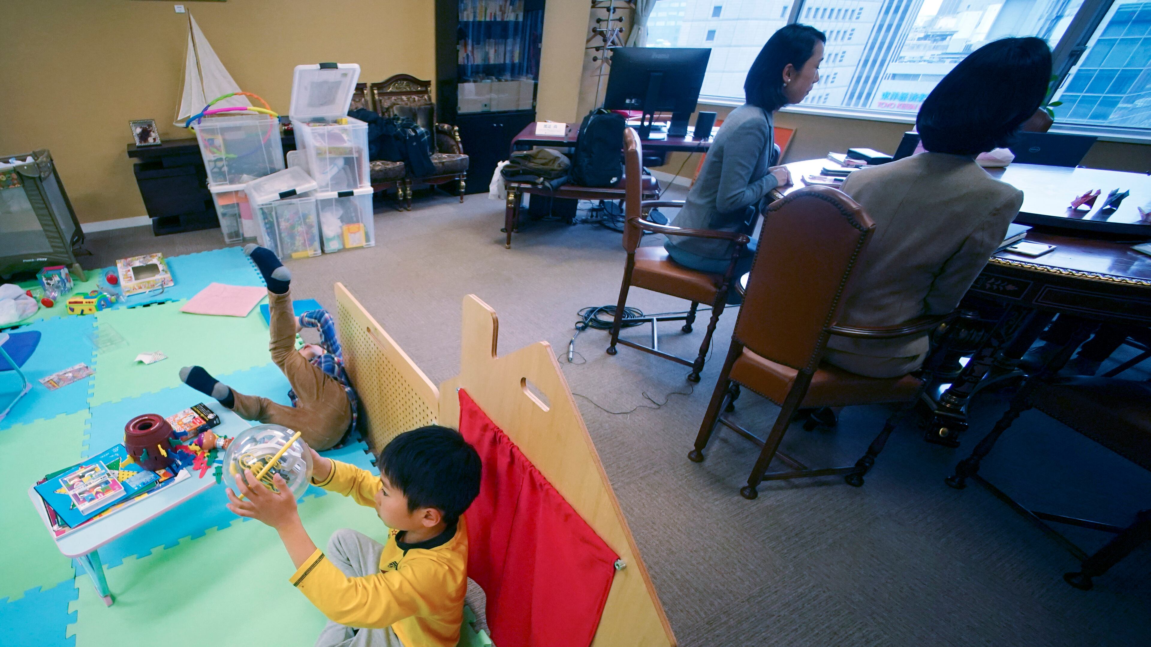 Keiko Kobayashi and Sachiko Aoki, both employees of the staffing services company Pasona Inc., work as their children entertain themselves at the company's headquarters Monday, March 2, 2020, in Tokyo. Many Japanese schools were shut down Monday and spring holidays began unexpectedly early for children as part of a government-led measure to prevent further escalation of the coronavirus. (AP Photo/Eugene Hoshiko)