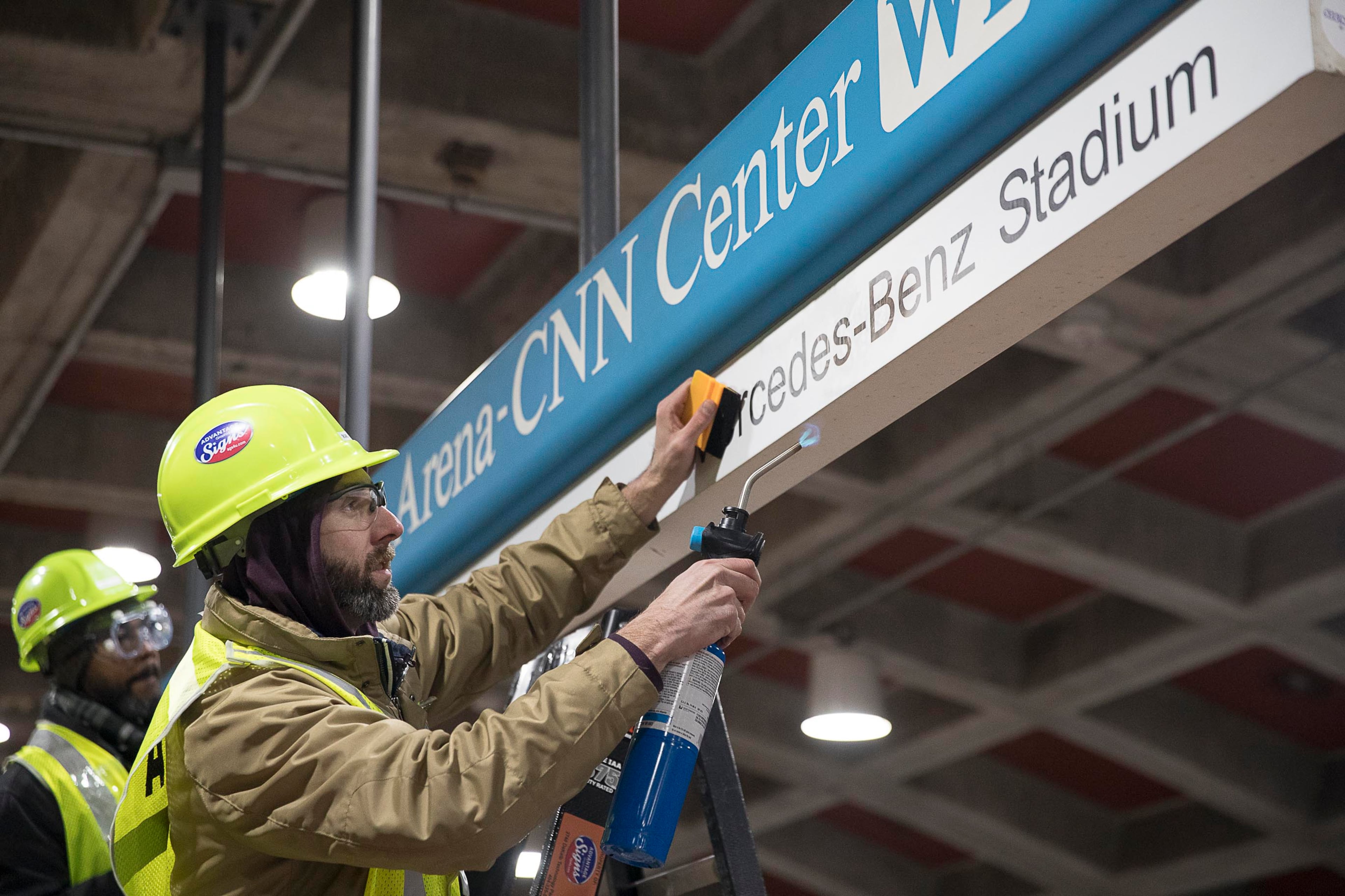 Tim Carl (second from left) of Advantage Graphics & Signs uses a torch to ensure the cohesiveness of the new Mercedes-Benz signage at the MARTA Dome/GWCC/Philips Arena/CNN Center Transit in Atlanta, Wednesday, Jan. 16, 2019. Advantage Graphics & Signs worked in the transit station on Wednesday to replace signage that mislabeled Atlanta's two newly named sport stadiums. (Alyssa Pointer/Alyssa.Pointer@ajc.com)