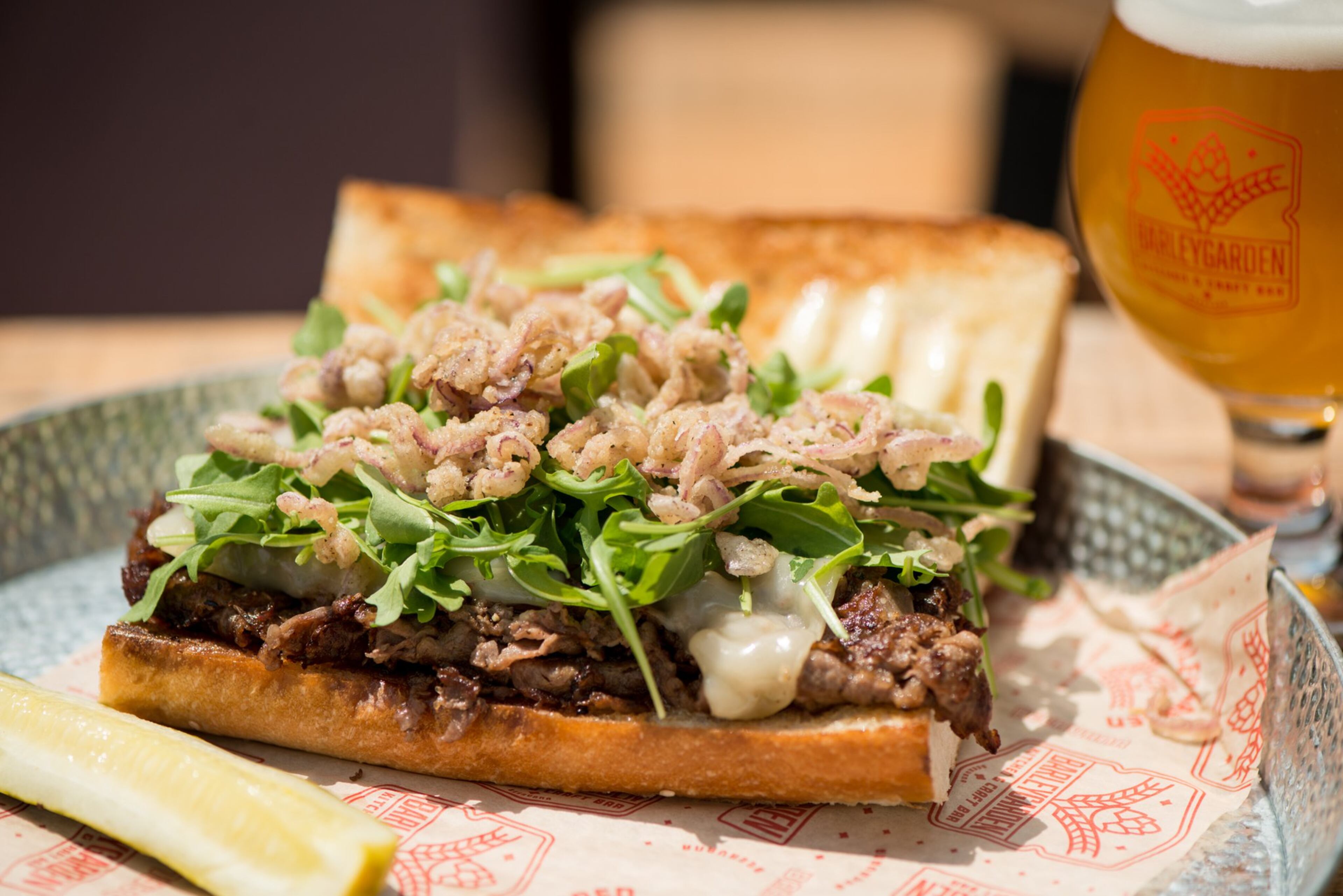 The Butchers Bun with ribeye steak, crispy onions, buttered sesame Cuban roll, gruyere, arugula, and roasted garlic aioli. Photo credit- Mia Yakel.