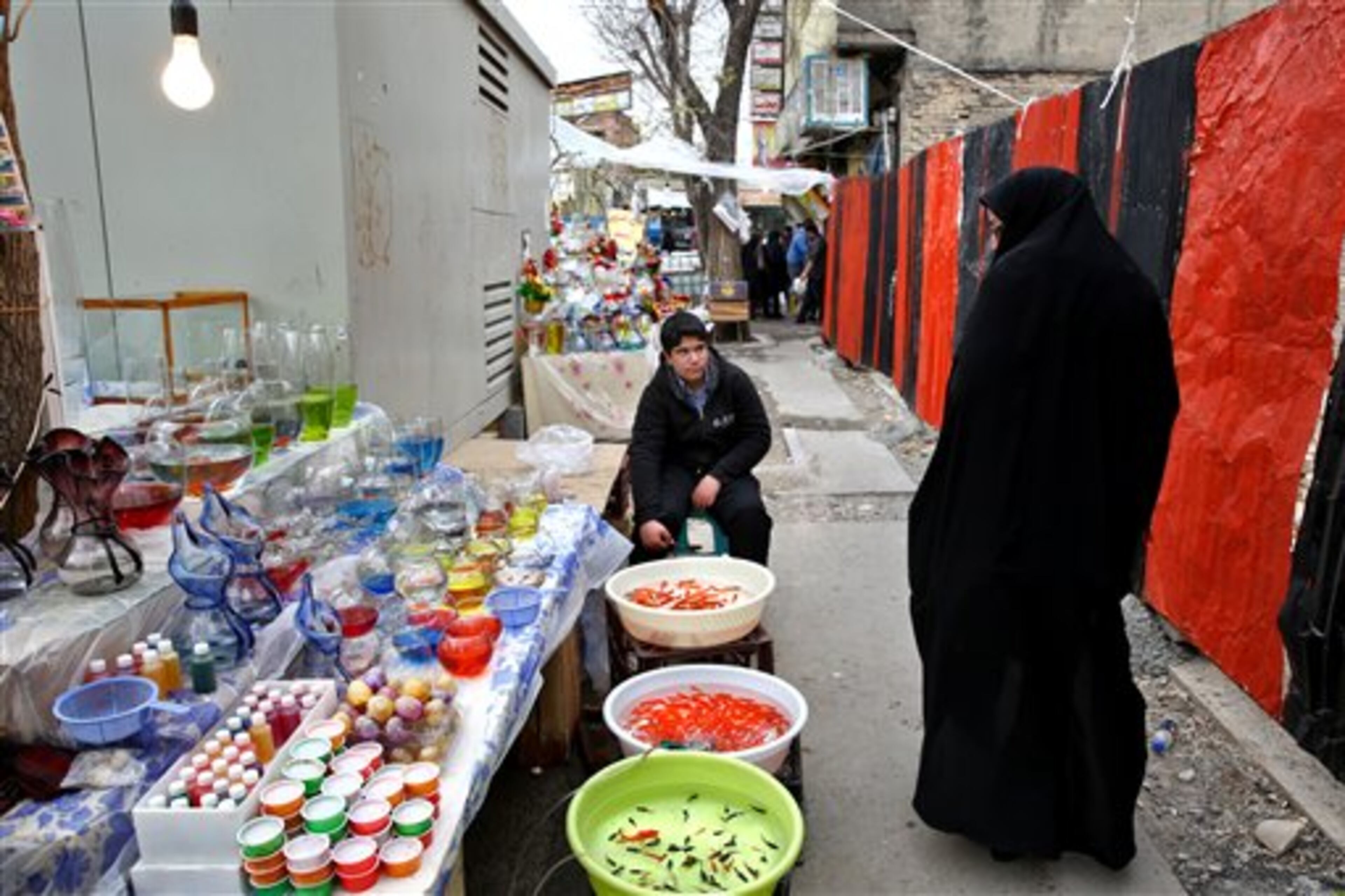 In this picture taken on Tuesday, March 18, 2014, an Iranian woman walks as a vendor sits next to his fish, a symbol of the Iranian New Year, ahead of the New Year, or Nowruz, in downtown Tehran, Iran. Nowruz which means "New Day" in Persian, marks the first day of spring and the beginning of the year on the Iranian calendar, which occurs exactly on the Spring Equinox, and usually begins on March 21 or the previous or following day. (AP Photo/Ebrahim Noroozi)