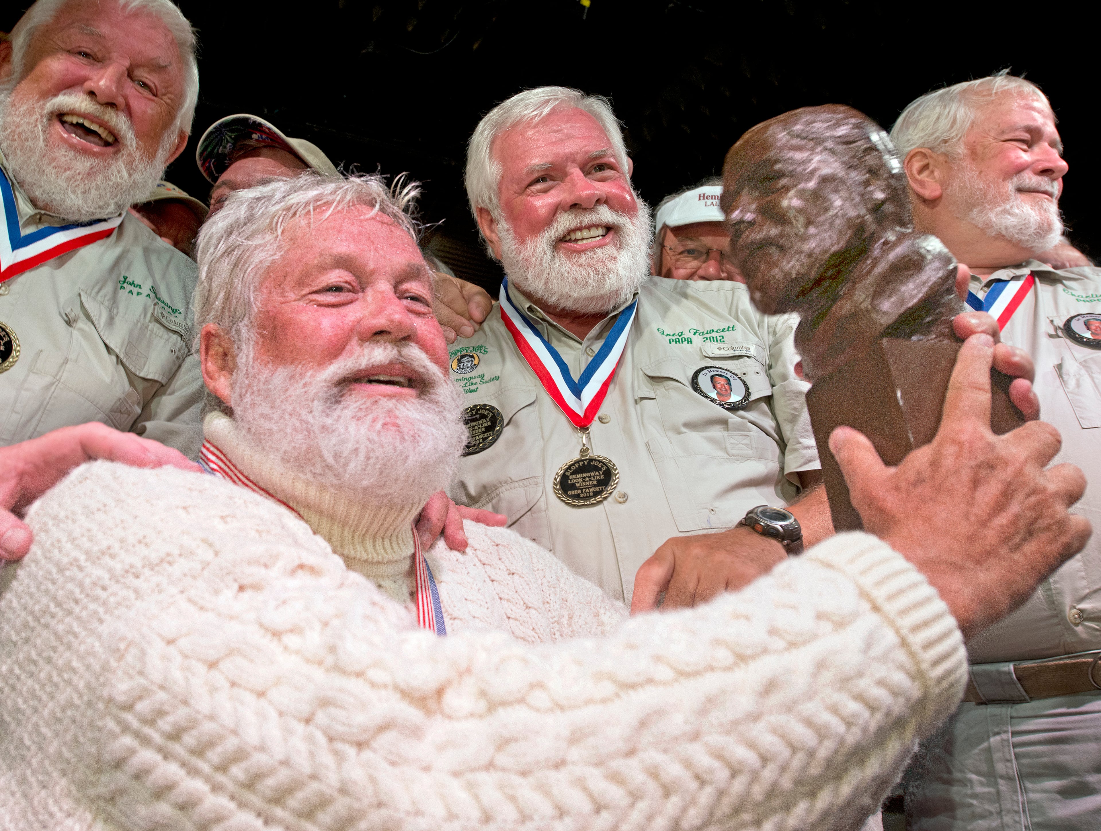 In this Saturday, July 19, 2014, photo provided by the Florida Keys News Bureau, Wally Collins holds a bust of Ernest Hemingway after winning the 2014 "Papa" Hemingway Look-Alike Contest at Sloppy Joe's Bar in Key West, Fla. A Phoenix resident, Collins won the title on his sixth try during the event that attracted 131 entrants. Collins is surrounded by previous winners including, from left, John Stubbings, Gregg Fawcett and Charlie Bicht. (AP Photo/Florida Keys News Bureau, Andy Newman)