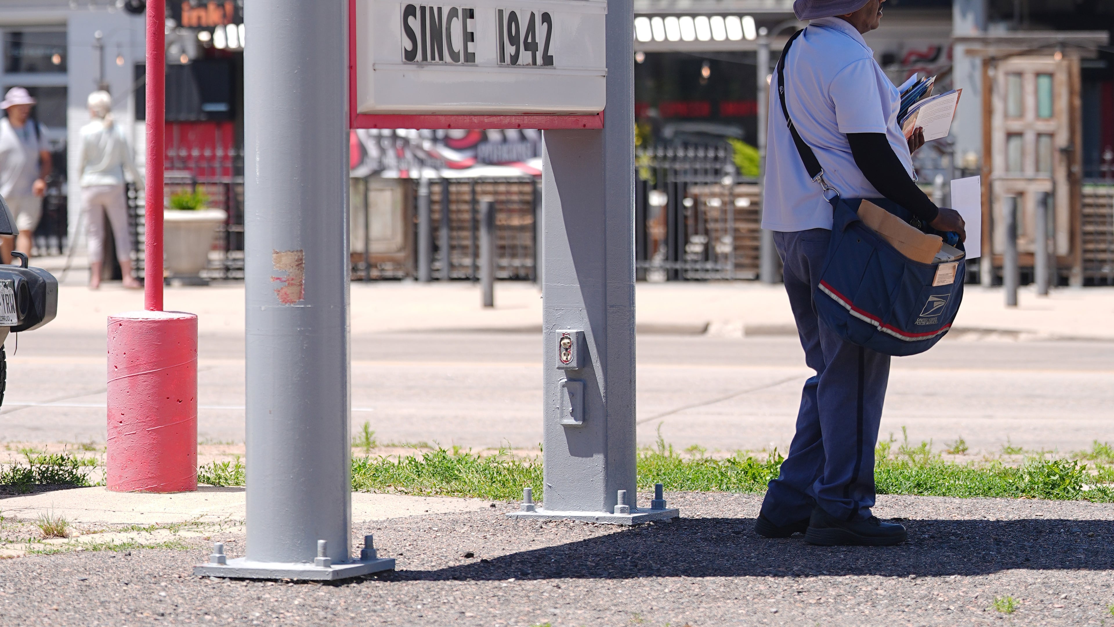 As the daytime high temperature soars into the 80s, a United States Postal Service postman keeps cool by standing in the shade of a gasoline station sign posting the per-gallon prices for the various grades of fuel available Thursday, June 4, 2026, in central Denver. (AP Photo/David Zalubowski)
