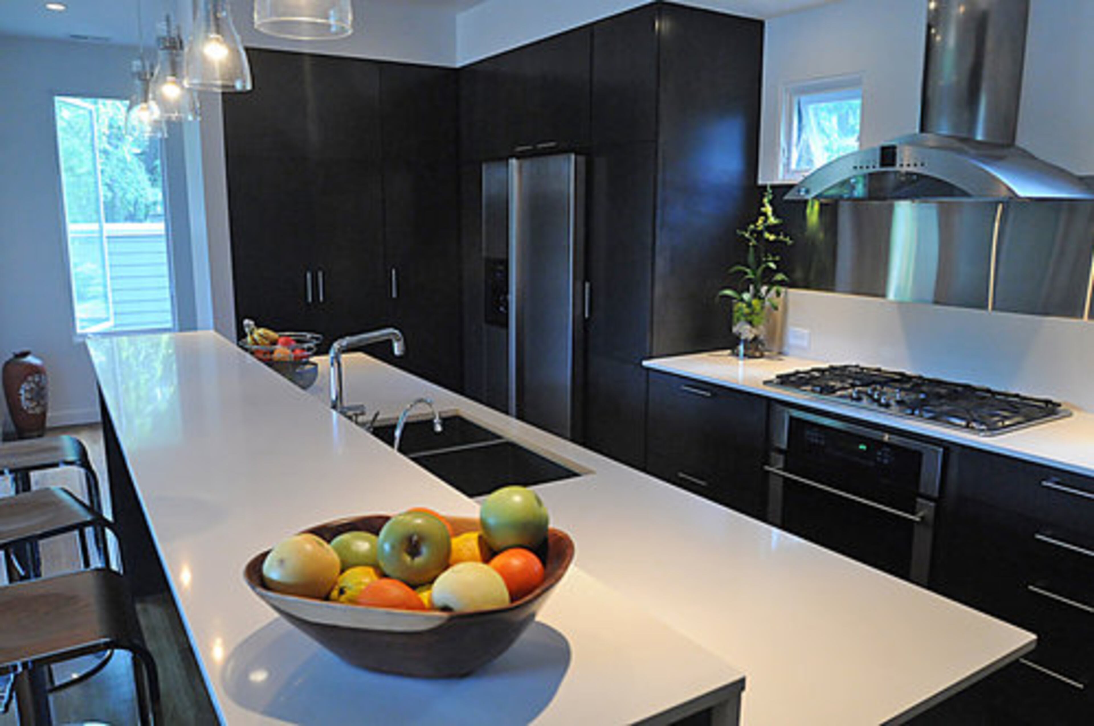 The kitchen features GE and Bosch appliances which are energy-efficient and blend seamlessly into the kitchen. The contrasting black-and-white color scheme is playfully highlighted with splashes of color by the placement of bowls of fruit.