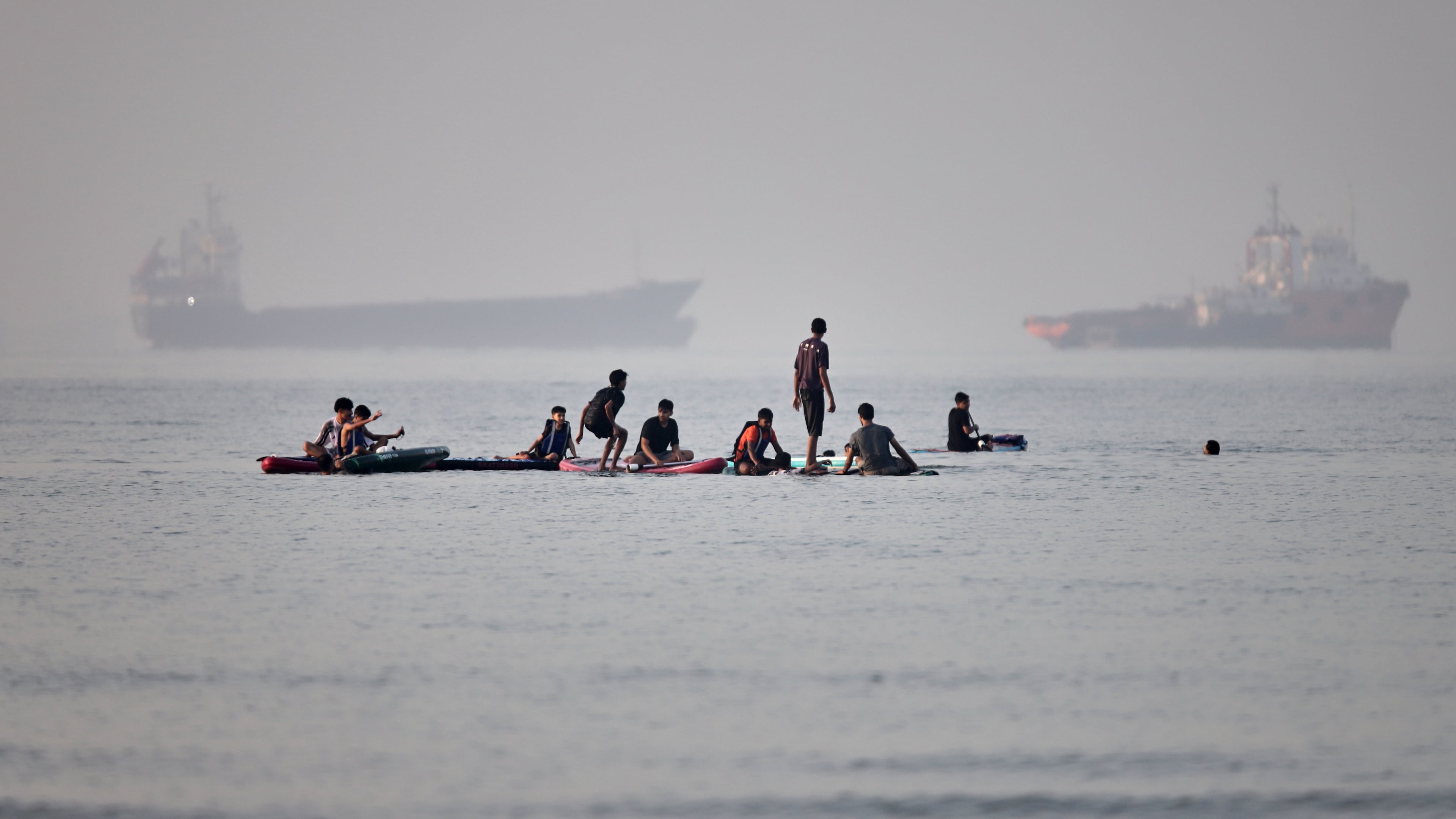 People gather on paddleboards in shallow water as cargo and service vessels are anchored in the Strait of Hormuz off Bandar Abbas, Iran, Monday, June 1, 2026. (Amirhosein Khorgooi/ISNA via AP)