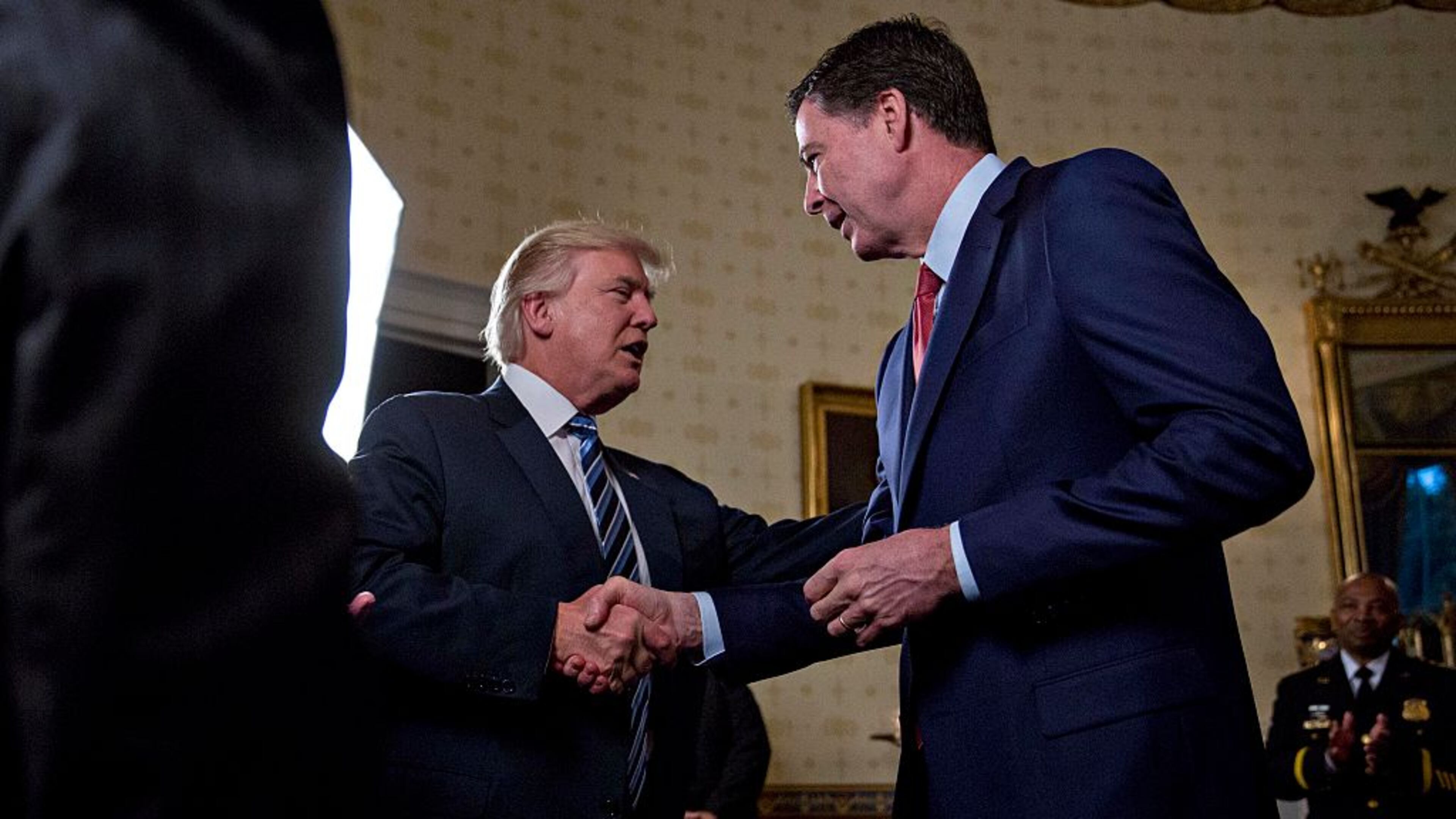 WASHINGTON, DC - JANUARY 22: U.S. President Donald Trump (C) shakes hands with James Comey, director of the Federal Bureau of Investigation (FBI), during an Inaugural Law Enforcement Officers and First Responders Reception in the Blue Room of the White House on January 22, 2017 in Washington, DC. Trump today mocked protesters who gathered for large demonstrations across the U.S. and the world on Saturday to signal discontent with his leadership, but later offered a more conciliatory tone, saying he recognized such marches as a "hallmark of our democracy." (Photo by Andrew Harrer-Pool/Getty Images)