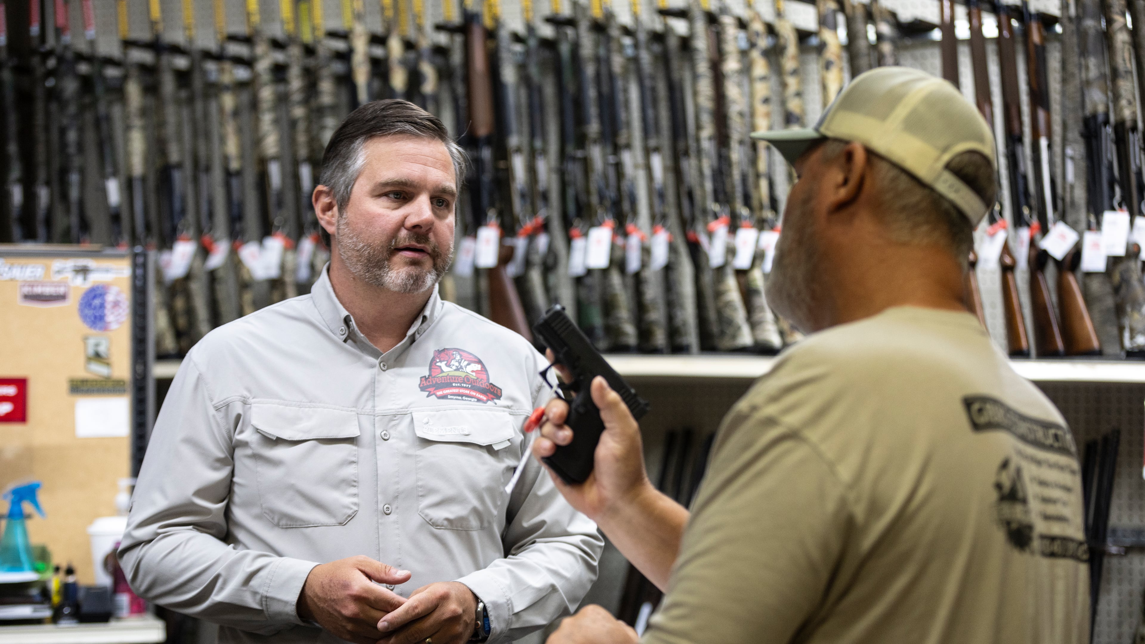 Adventure Outdoors general manager and part-owner Eric Wallace, left, helps Bobby Gibbs decide on a potential gun purchase in Smyrna on Tuesday, July 23, 2024. Sales are up substantially, according to Wallace. “A lot of our customers are saying that if the Secret Service, which is known to be one of the best law enforcement agencies in the world, can’t protect a former president, how is our government going to protect us if something serious were to happen?” Wallace said. (Steve Schaefer / AJC)