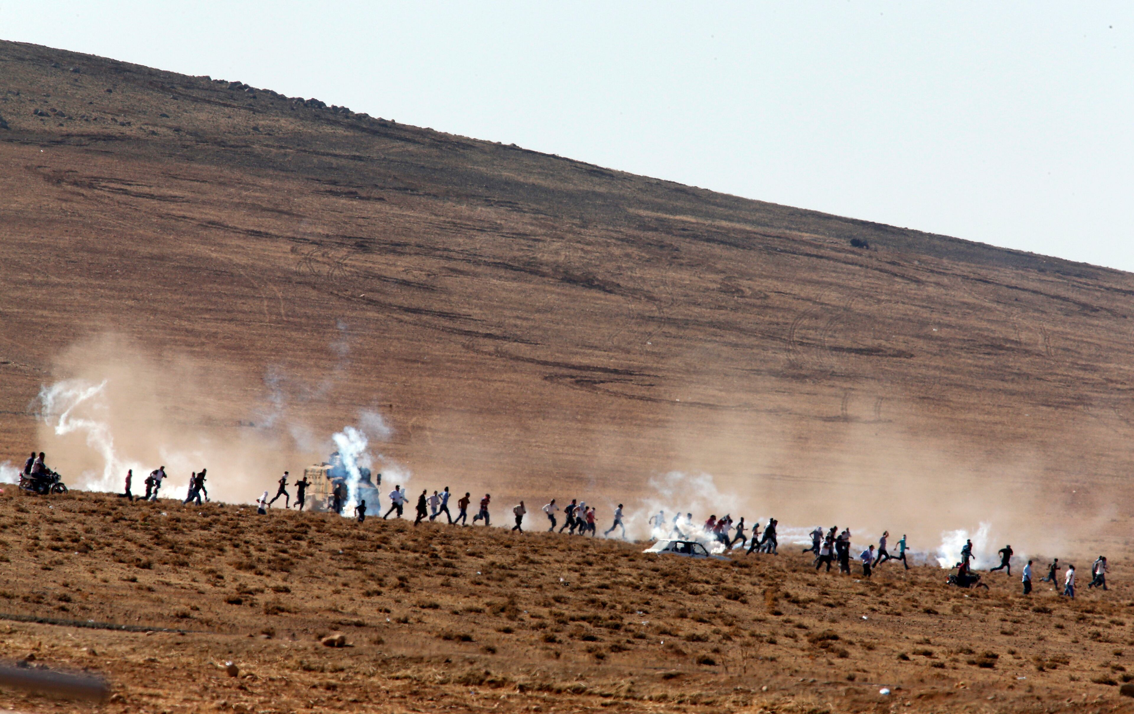 Turkish Kurds run in the outskirts of Suruc, at the Turkey-Syria border, to avoid the effect of tear gas fired by Turkish forces to disperse them after they gathered as fighting intensified between Syrian Kurds and the militants of Islamic State group, in nearby Kobani, Syria, Tuesday, Oct. 7, 2014. Kobani, also known as Ayn Arab and its surrounding areas have been under attack since mid-September, with militants capturing dozens of nearby Kurdish villages.(AP Photo/Lefteris Pitarakis)