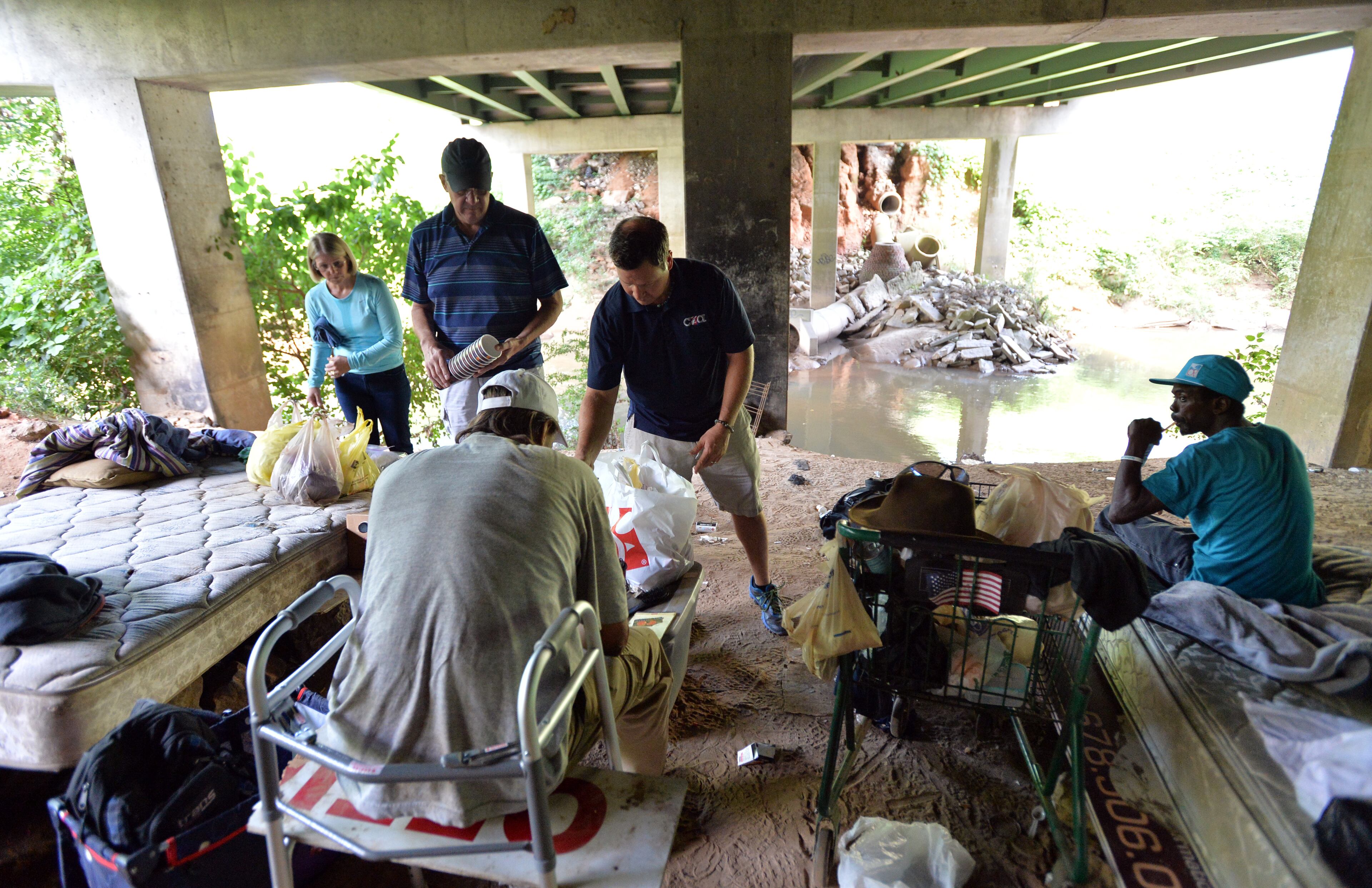 Turner (standing center), executive director of Contribute2America, is joined by Bill and Chris Beagle as he delivers food, supplies and personal hygiene items to homeless people living beneath Buford Highway. HYOSUB SHIN / HSHIN@AJC.COM