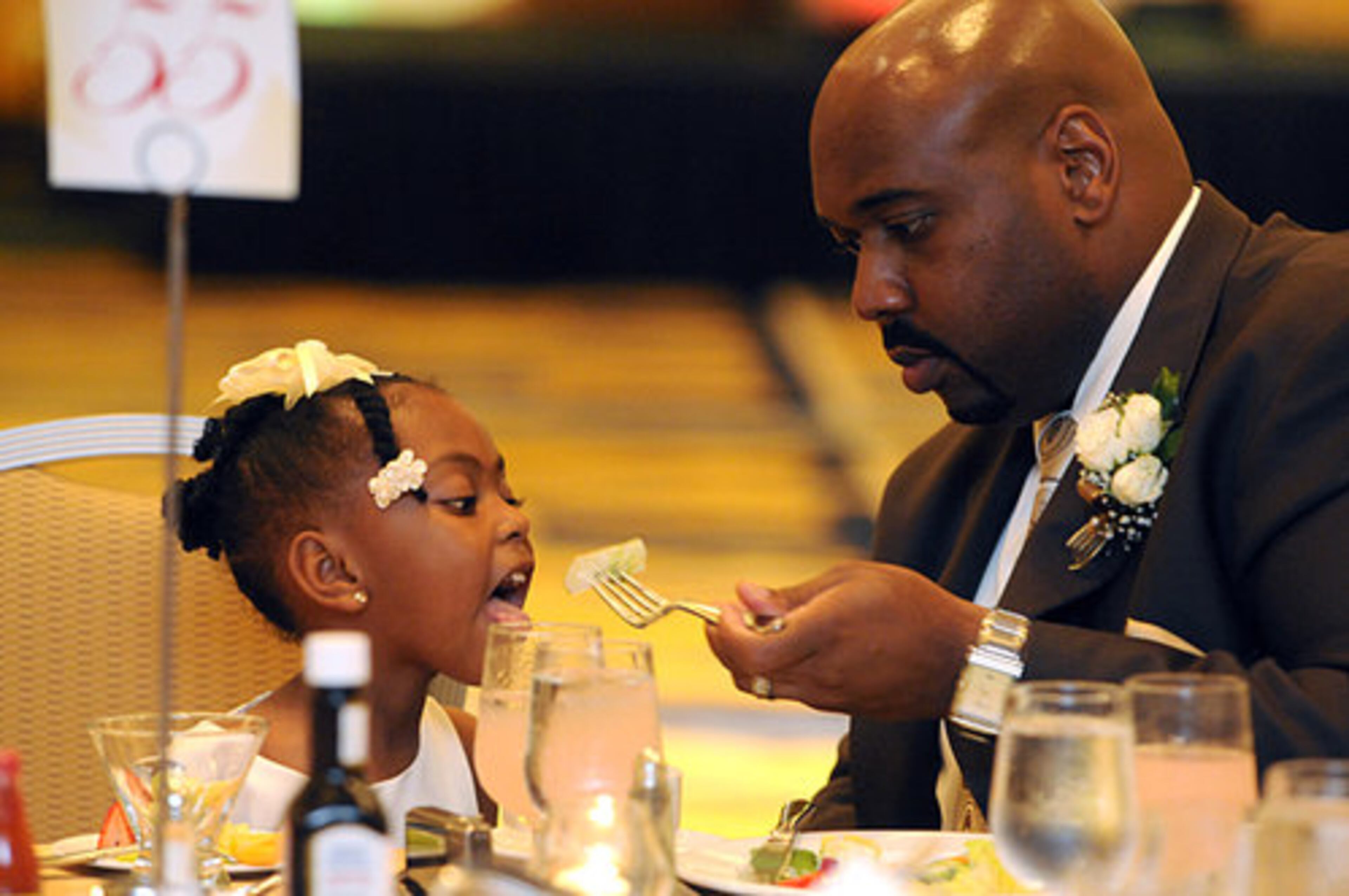 (From left) Morgan Kenneybrew, 3, gets a bite of food from her father Andre Kenneybrew, 34, (both from Conyers.) This is their first year attending the dance and Kenneybrew says his favorite part of the night, thus far, was the first dance.