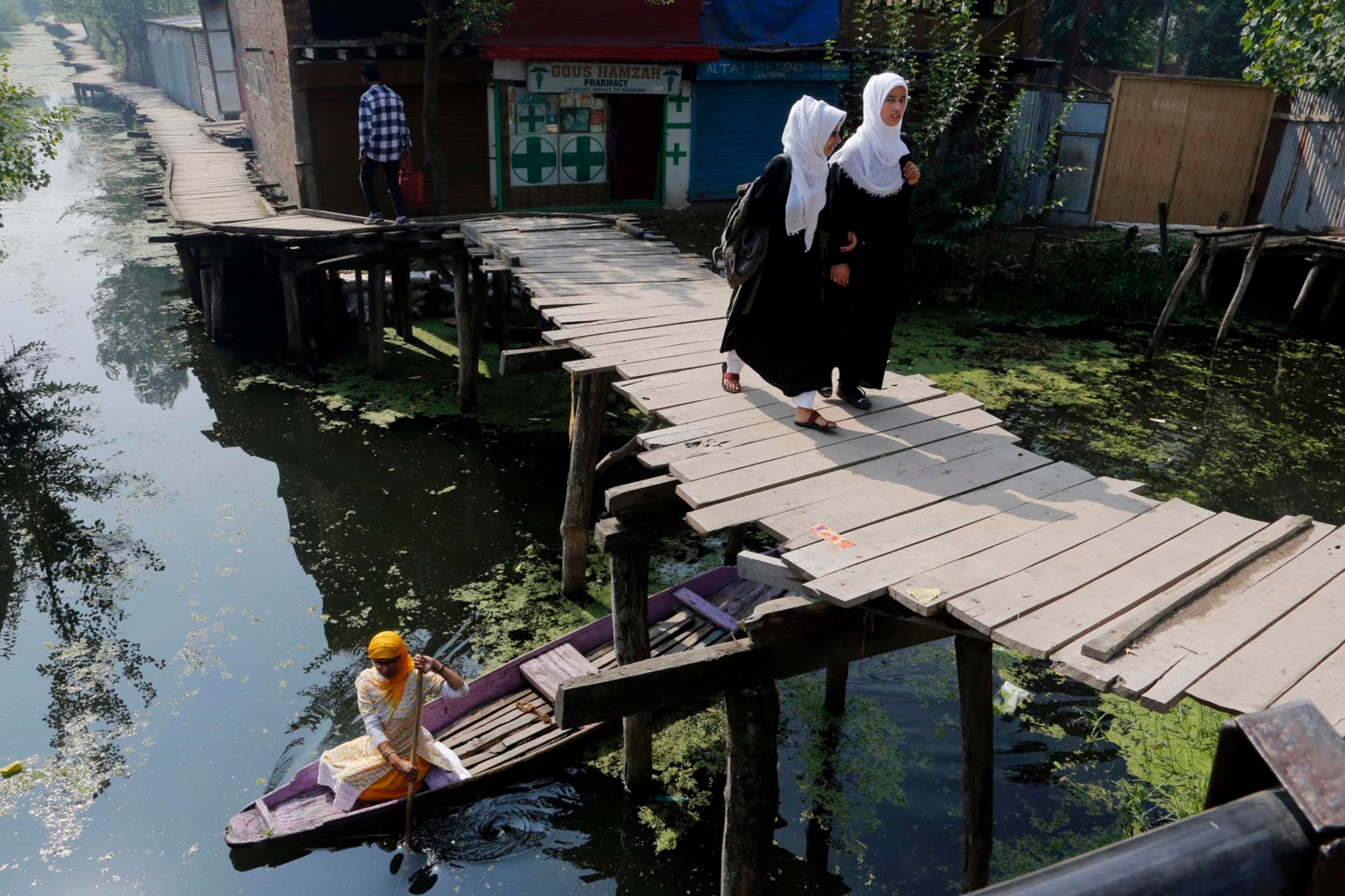 Kashmiri school girls cross a wooden footbridge on their way to school as a woman rows her Shikara, or traditional Gondola, underneath, on the Dal Lake in Srinagar, Indian controlled Kashmir, Thursday, July 27, 2017. Shikaras are small wooden boats used by locals living around water bodies in Kashmir for multiple purposes, including transportation of people, fishing, carrying harvest of aquatic vegetation. Decorated Shikaras provide a water taxi service to see the sights around the Lakes and to approach houseboats moored on the lake periphery. (AP Photo/Mukhtar Khan)