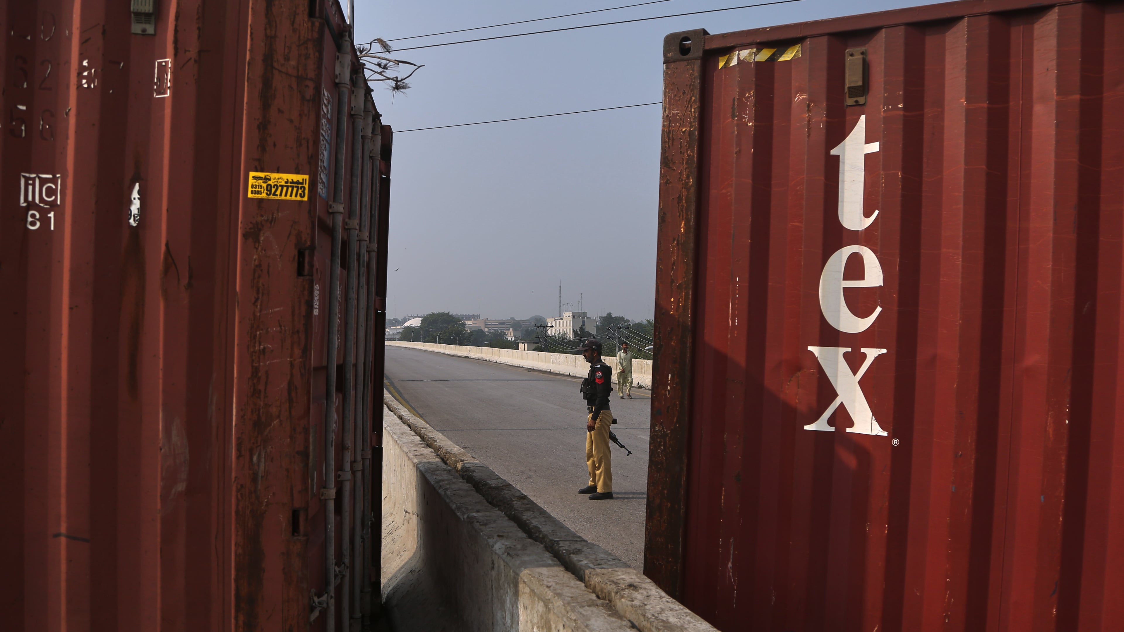 A police officer stands guard at a road barricaded with shipping containers by authorities ahead of a protest by the supporters of imprisoned former Prime Minister Imran Khan demanding his release, in Peshawar, Pakistan, Sunday, Oct. 11, 2026. (AP Photo/Mohammad Zubair)