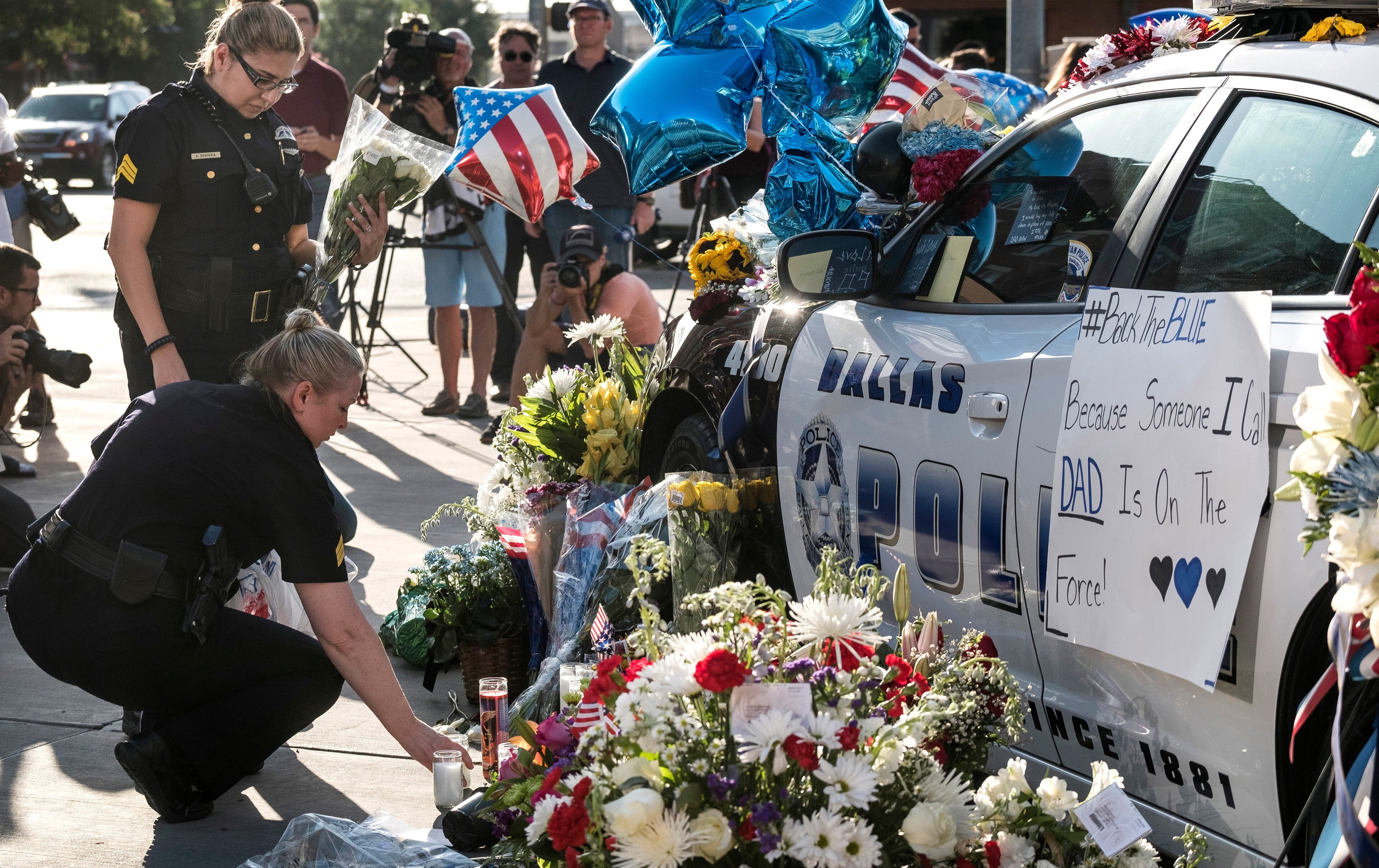 July 8, 2016 - Sgt. Amanda Renteria, left, and partner Sgt. Laura Browning, squatting, place flowers on a memorial of flowers, gifts and cards covering Dallas patrol cars in front of the Dallas Police department headquarters in Dallas, Texas, on Friday, July 8, 2016. Five officers were killed, six officers wounded along with two civilians were shot by suspected sniper Micah Johnson. RODOLFO GONZALEZ / AUSTIN AMERICAN-STATESMAN