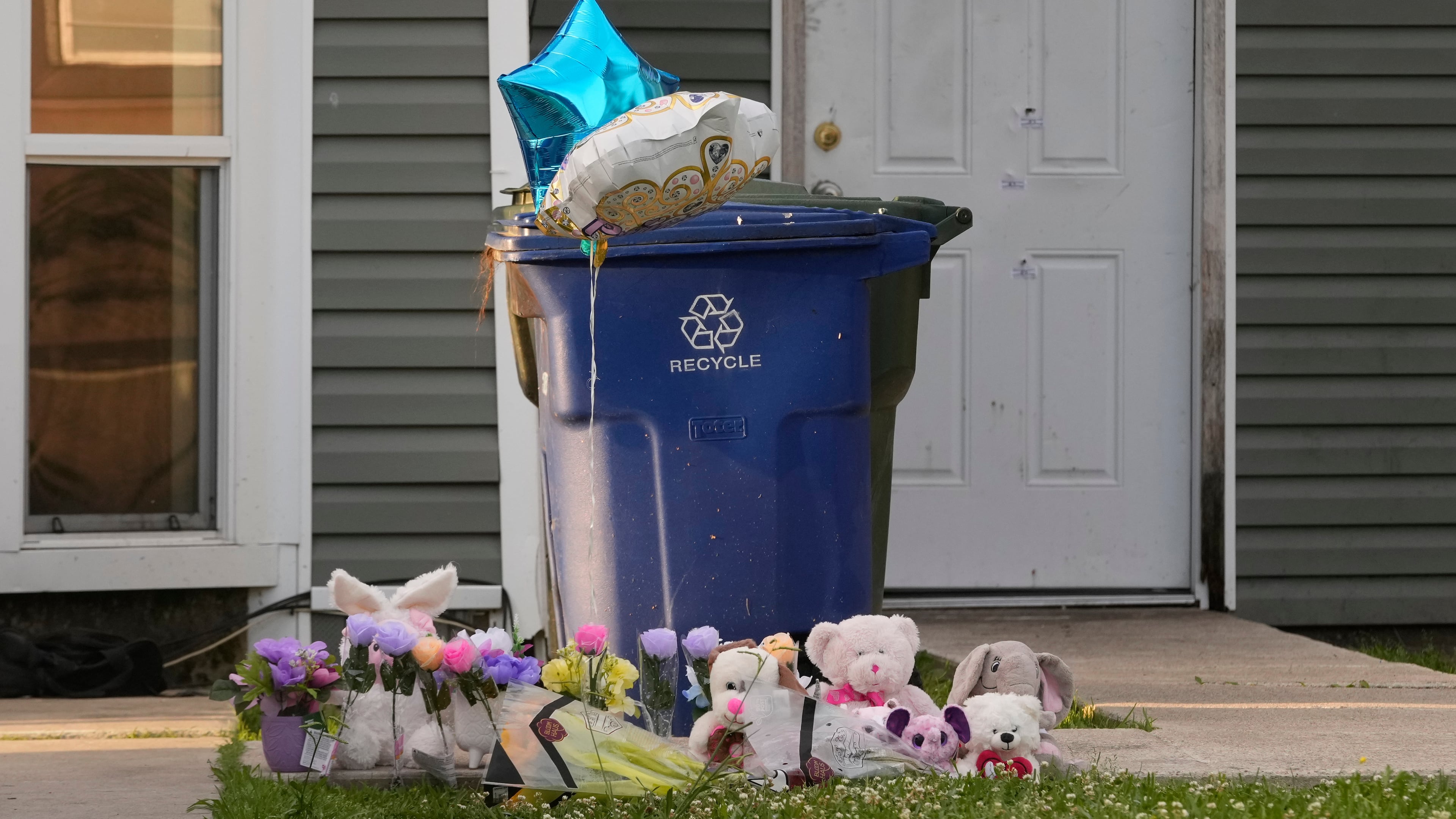 A makeshift memorial is growing on the front lawn of a home as the door in the background shows bullet holes and evidence markers where children were killed during a mass shooting the day before in Shreveport, La., Monday, April 20, 2026. (AP Photo/Gerald Herbert)