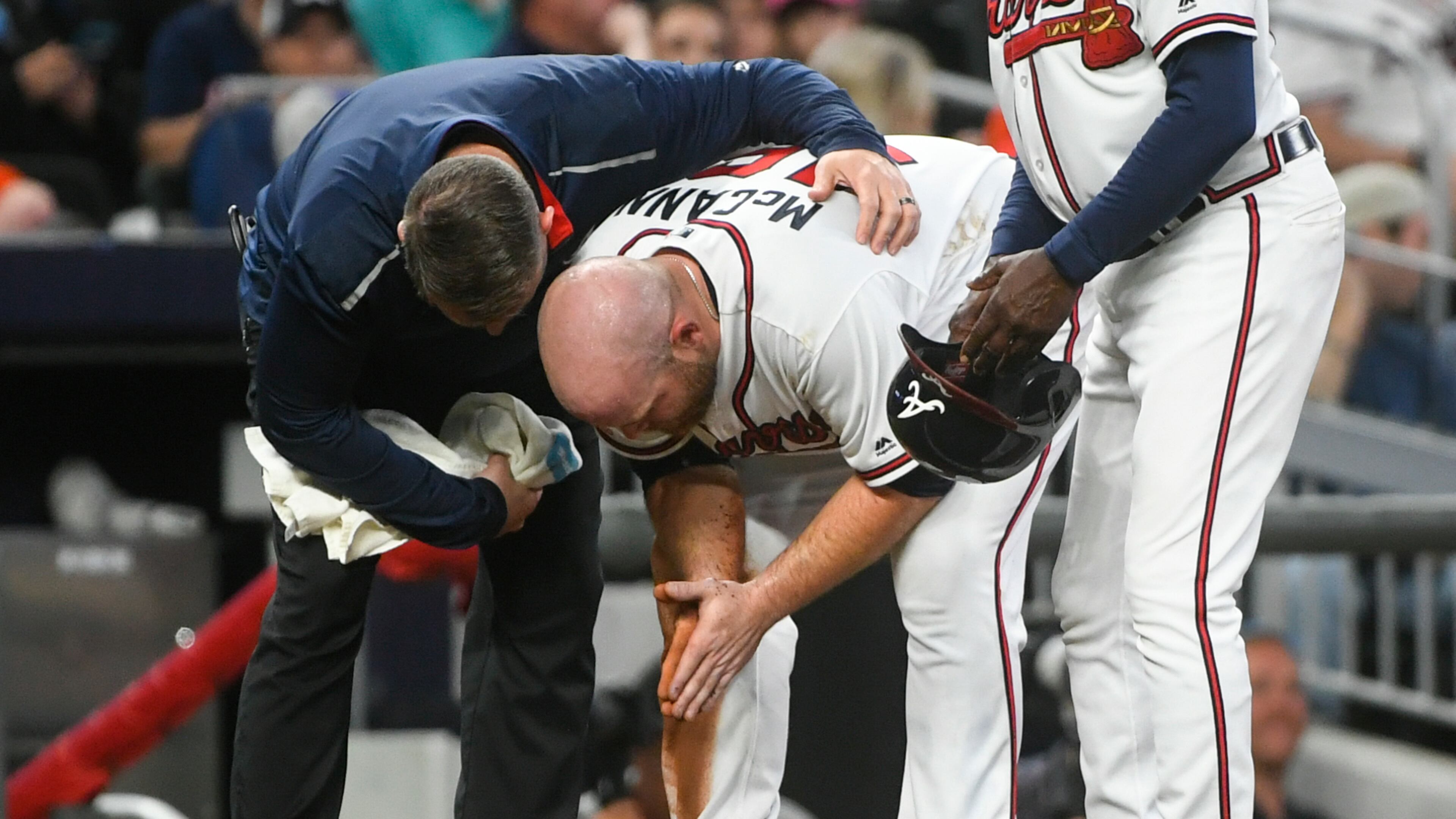 Braves catcher Brian McCann is tended to by trainer Mike Frostad, left, after being thrown out sliding into third base by Miami Marlins catcher Jorge Alfaro on a bunt by Kyle Wright during the fifth inning. (AP Photo/John Amis)