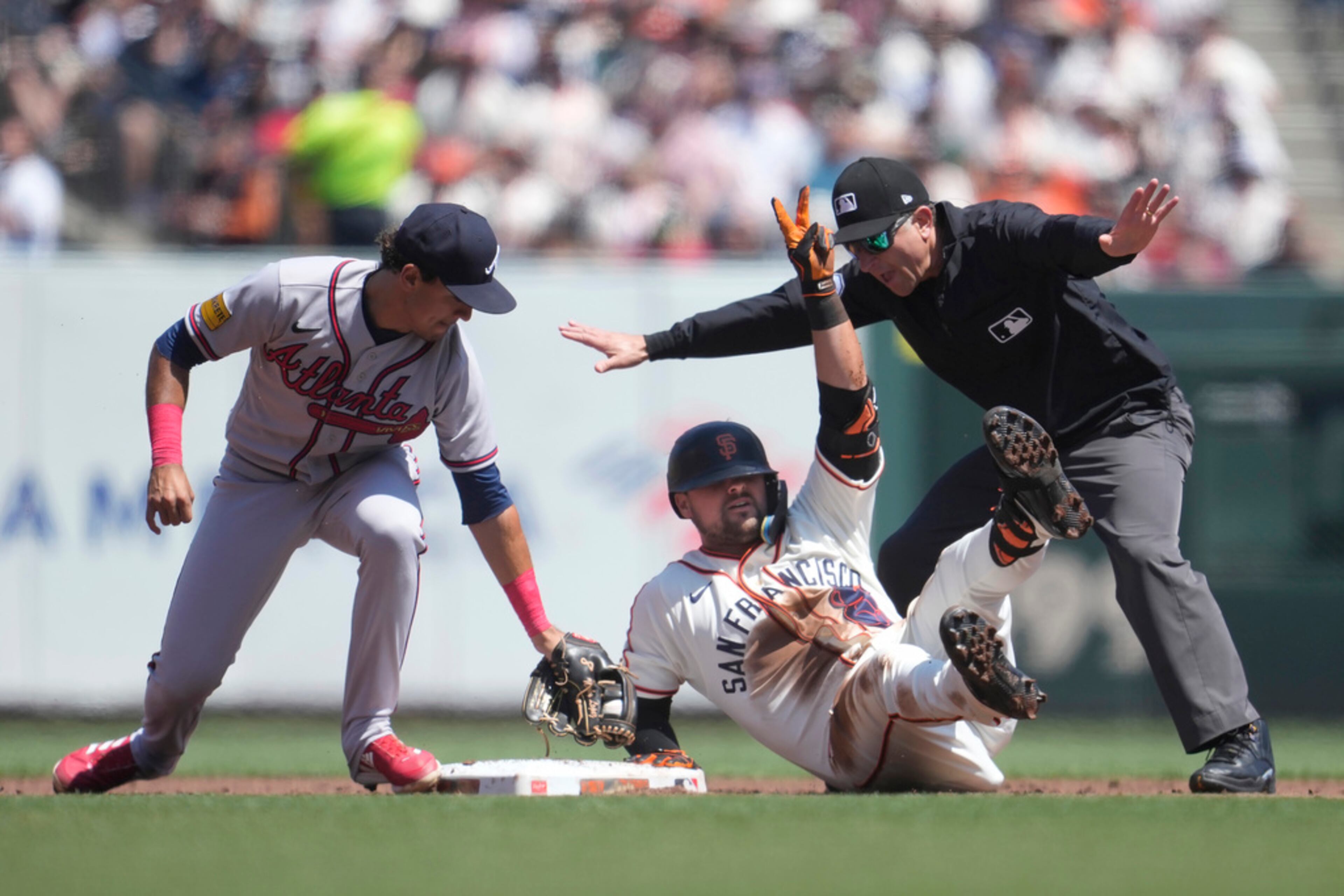 San Francisco Giants' J.D. Davis, bottom, gestures under umpire Chris Guccione, right, and next to Atlanta Braves second baseman Nicky Lopez after hitting a double during the second inning of a baseball game in San Francisco, Saturday, Aug. 26, 2023. (AP Photo/Jeff Chiu)