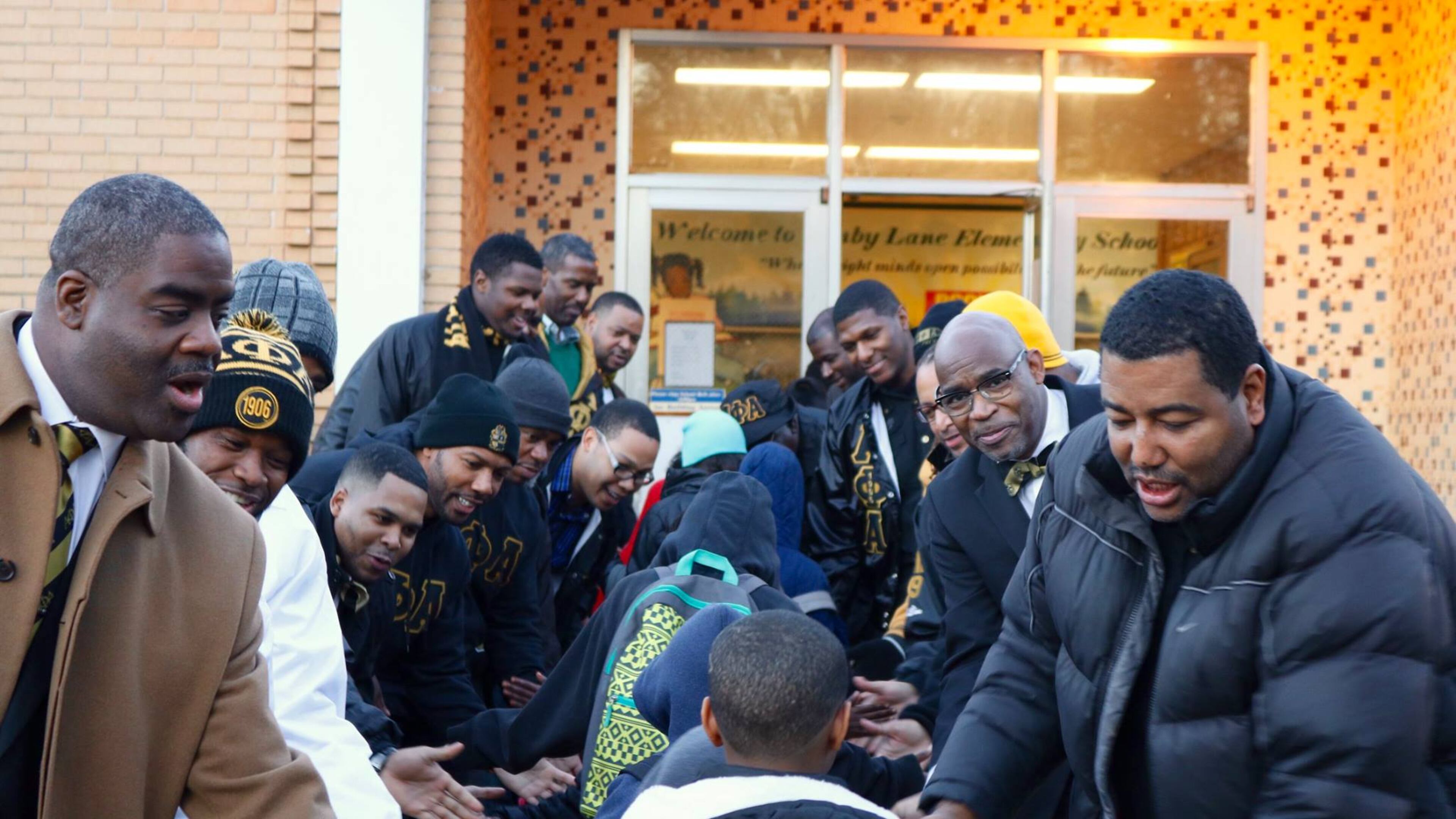 Brothers of the Nu Mu Lambda (DeKalb) Chapter of Alpha Phi Alpha greet local elementary school students with handshakes, high fives, hugs, and words of encouragement as they begin their day.