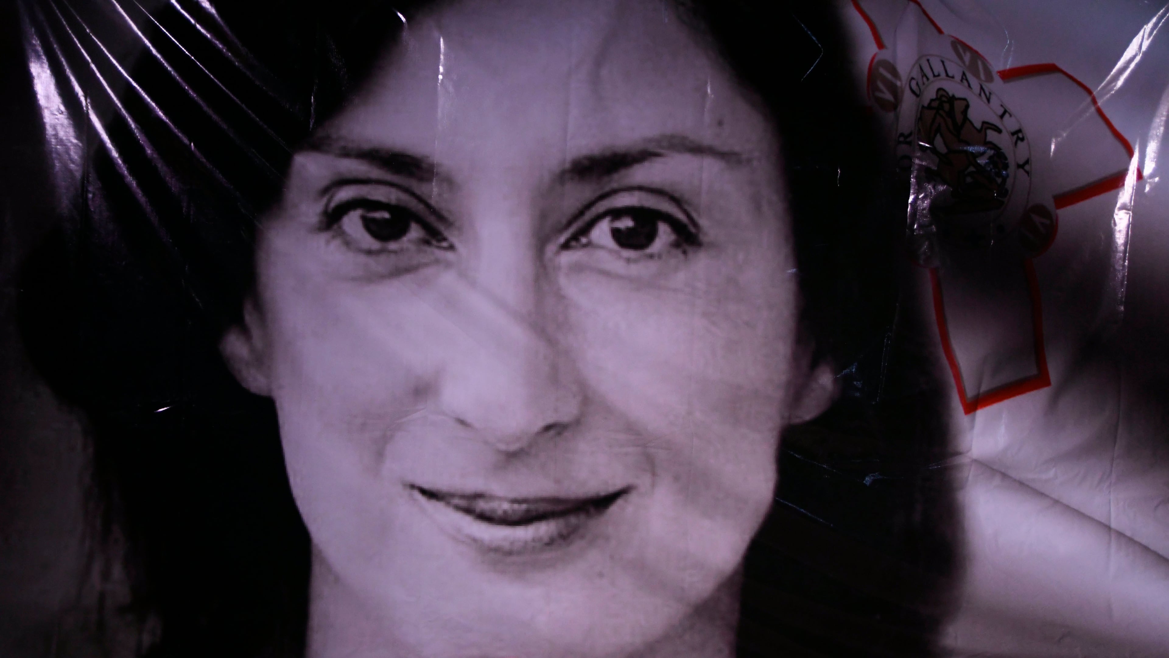 FILE - Flowers and a candle lie in front of a portrait of slain investigative journalist Daphne Caruana Galizia during a vigil outside the law courts in Valletta, Malta, Oct. 16, 2018. (AP Photo/Jonathan Borg, File)