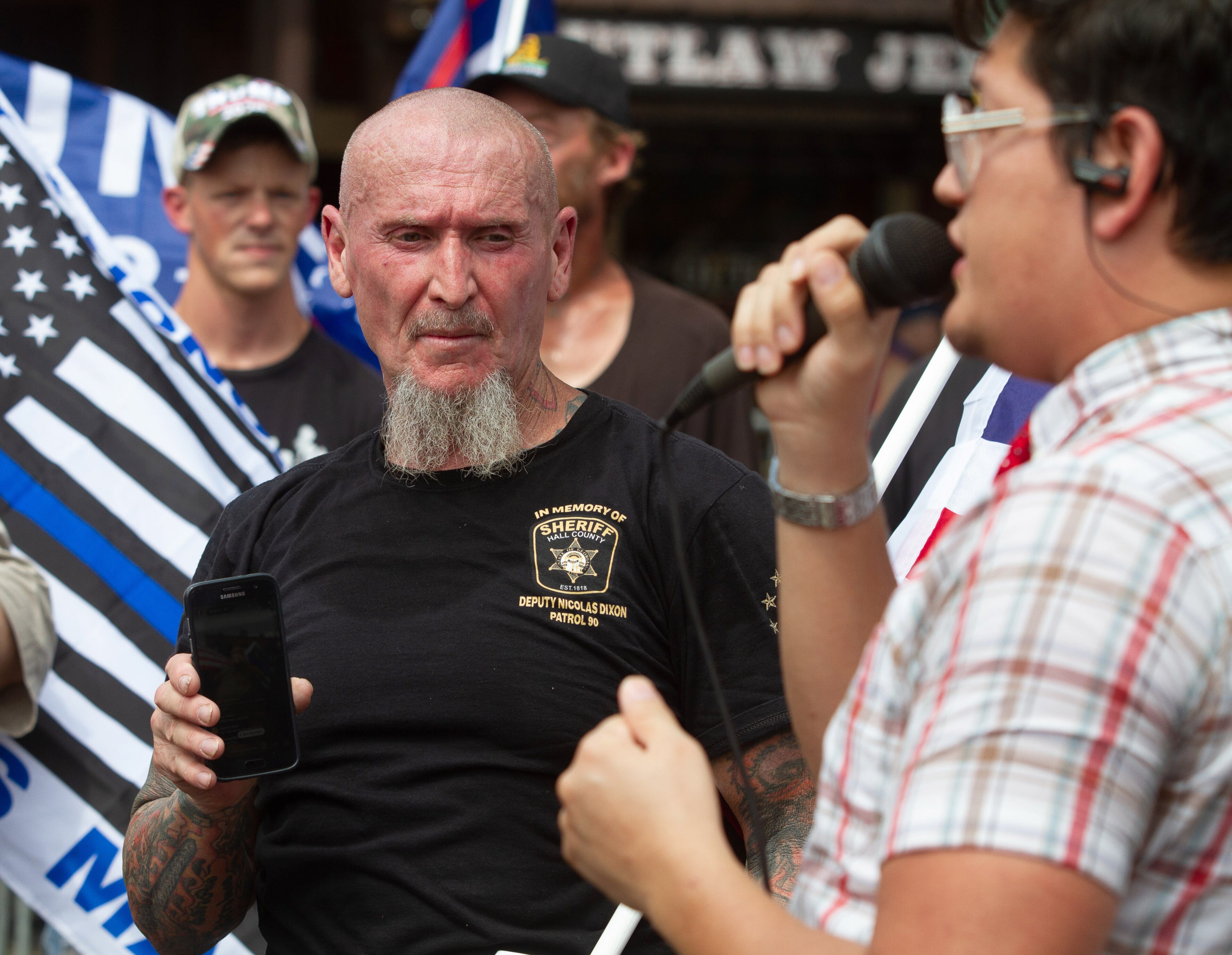 Chester Doles (left), the principal rally organizer, listens to Jovi Val speak to a small crowd in Dahlonega on Saturday, September 14, 2019. STEVE SCHAEFER / SPECIAL TO THE AJC